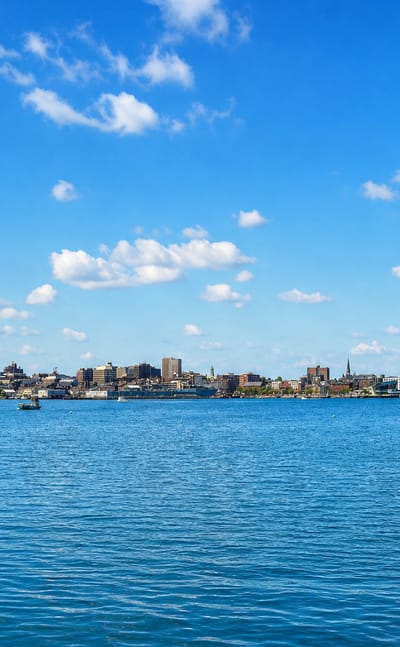Portland, Maine's low waterfront skyline seen across Casco Bay under a bright blue summer sky.