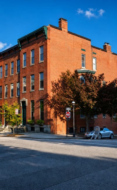 A sunlit block of three-story red-brick rowhouses on a quiet street corner in Baltimore's Bolton Hill.