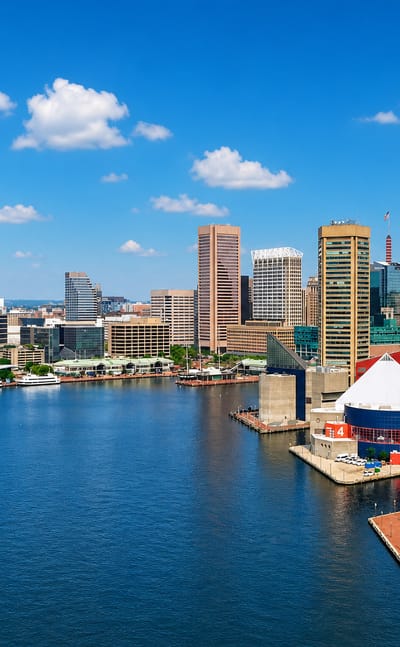 Baltimore Inner Harbor with marina boats, the small red lighthouse and downtown skyline under a blue sky