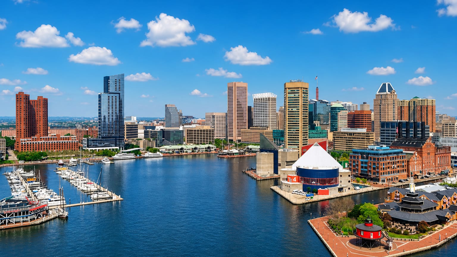 Baltimore Inner Harbor with marina boats, the small red lighthouse and downtown skyline under a blue sky