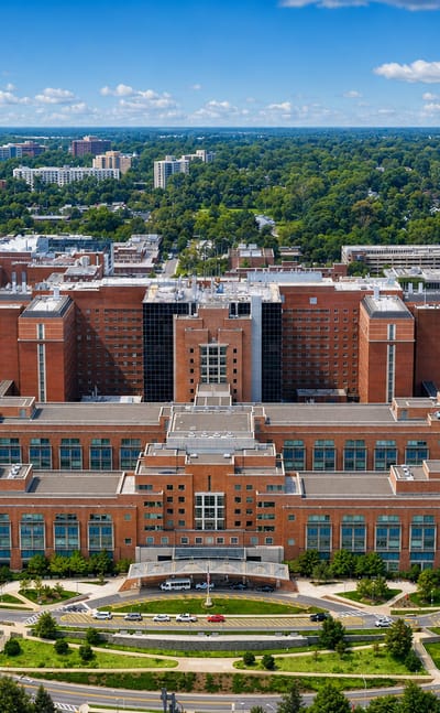 The red-brick NIH Clinical Center campus in Bethesda, Maryland, framed by green suburbs under a blue sky.