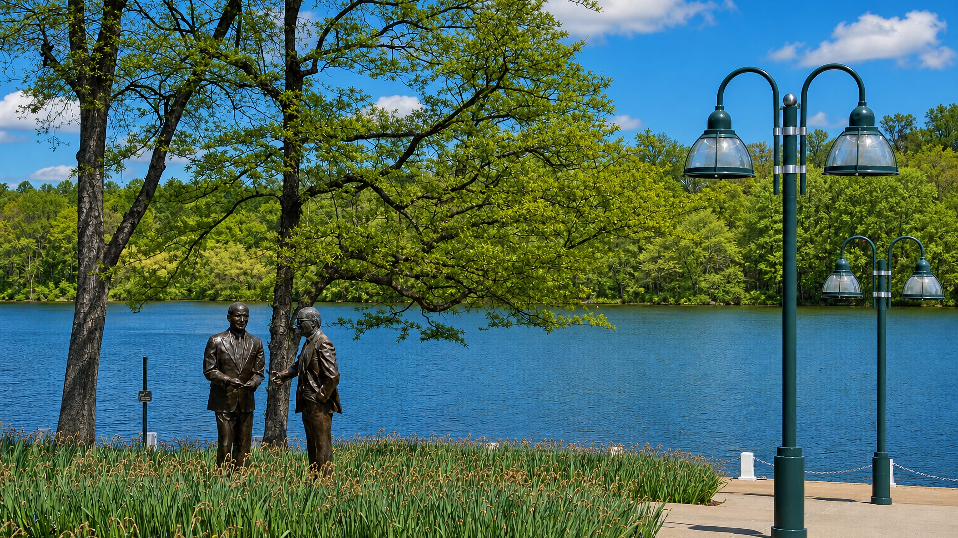 Bronze statues beside Lake Kittamaqundi on Columbia's lakefront in Maryland, framed by trees and lamp posts