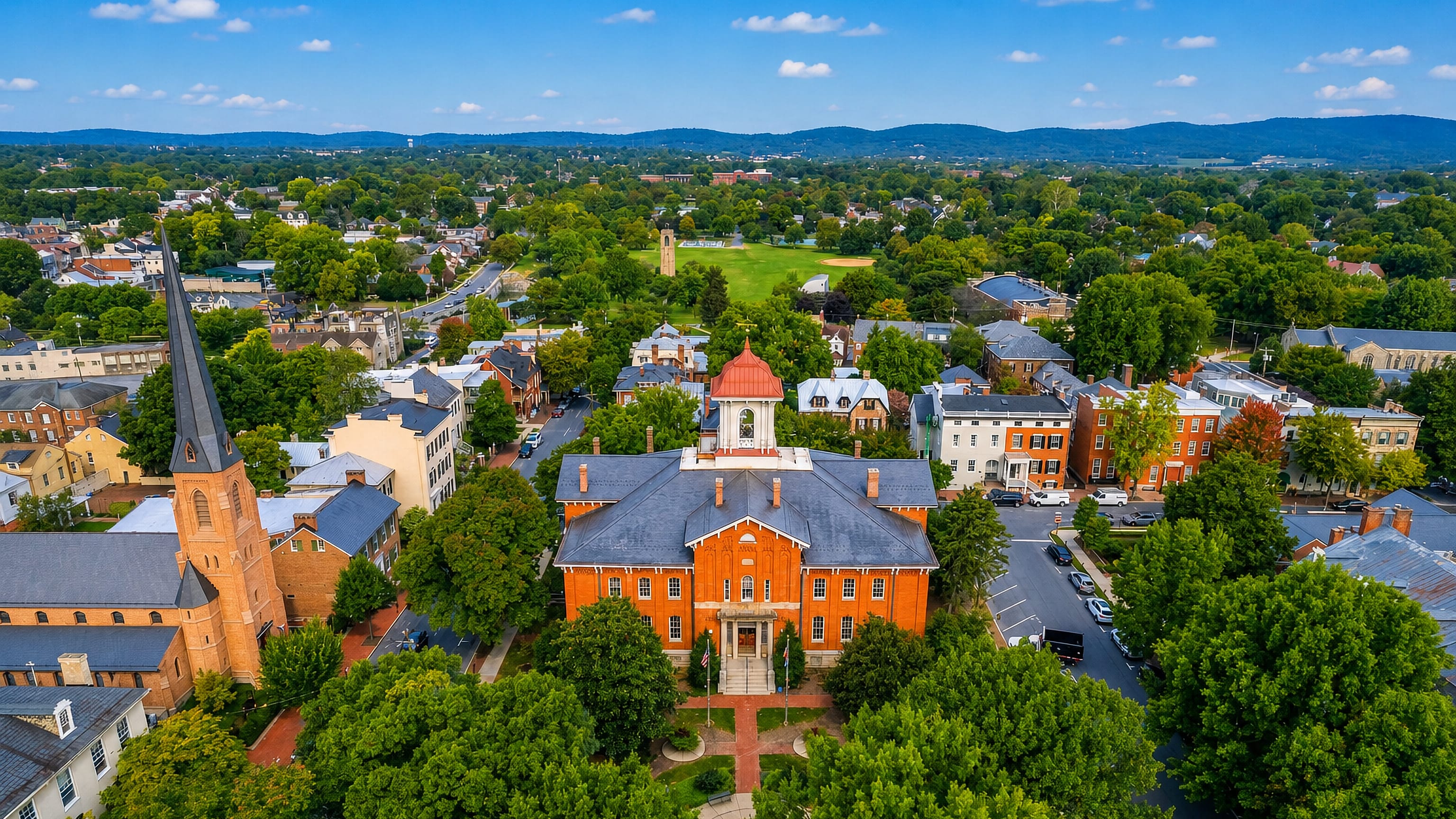 Aerial view of downtown Frederick, Maryland, its clustered church spires and brick courthouse cupola below Catoctin ridges.