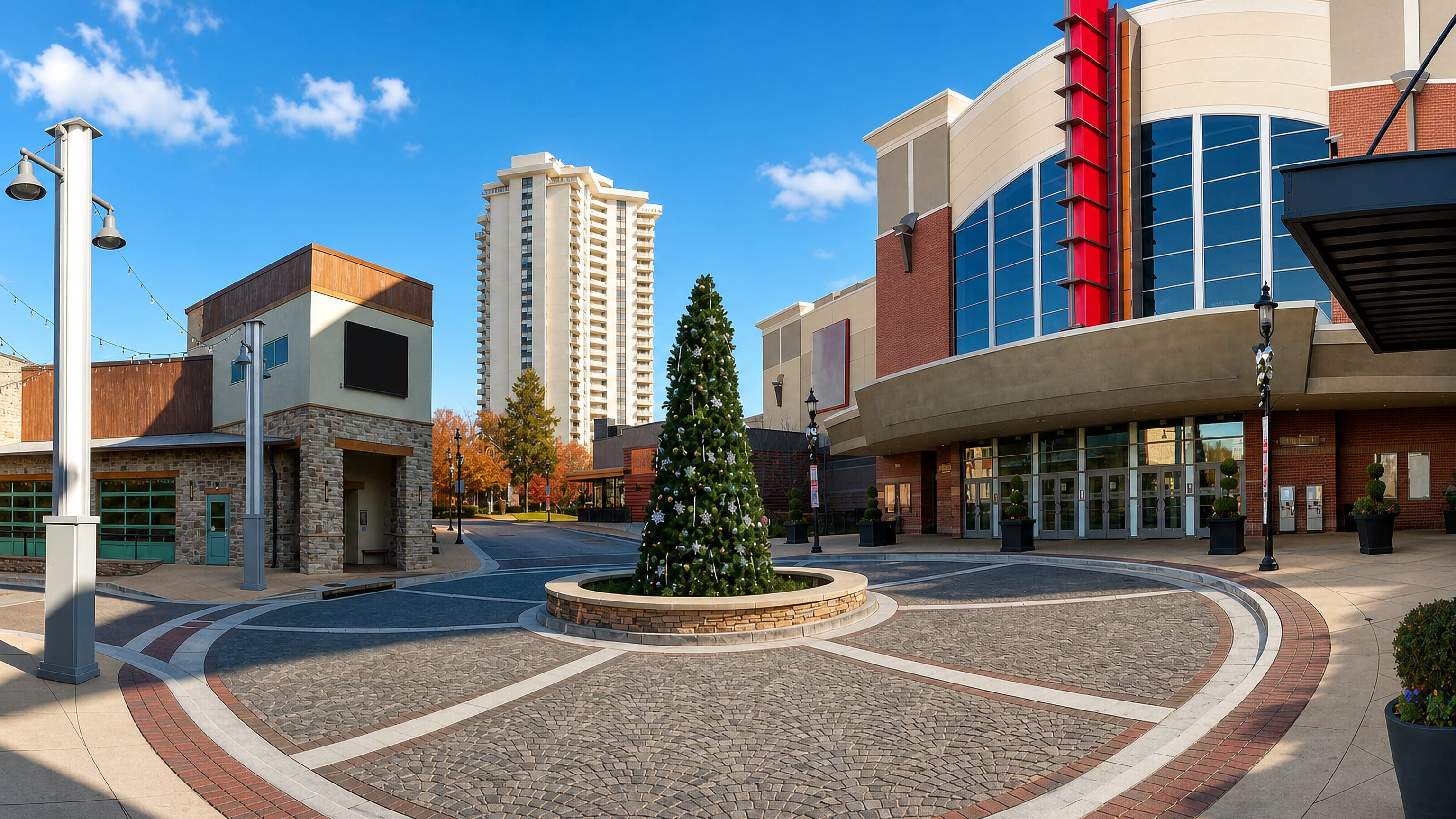 Sunlit brick-paved plaza with a cinema entrance, holiday tree and a residential high-rise beyond in Towson, Maryland.