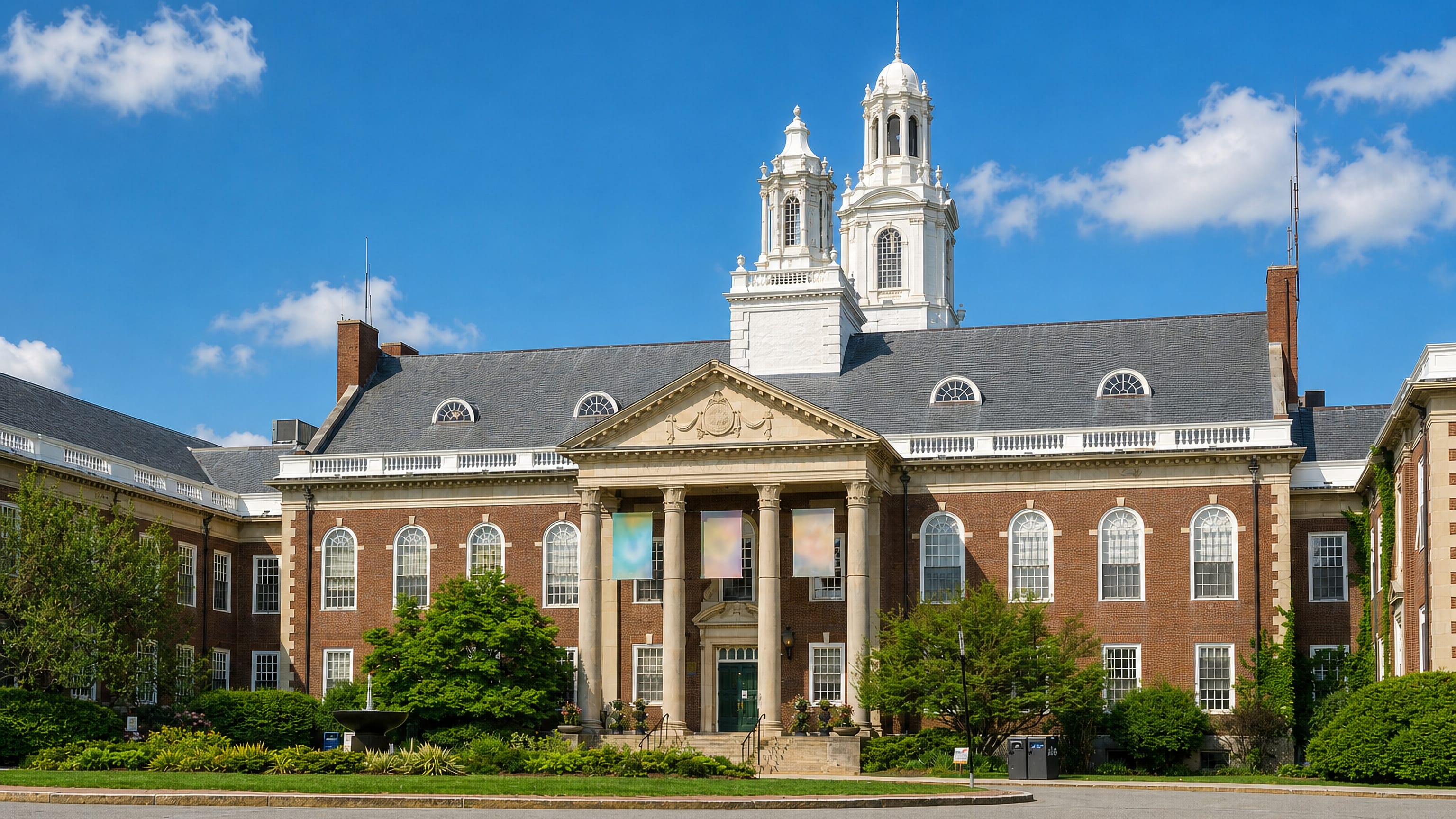 Newton City Hall, a brick Georgian-style building with a white cupola, above lawns in Newton, Massachusetts.