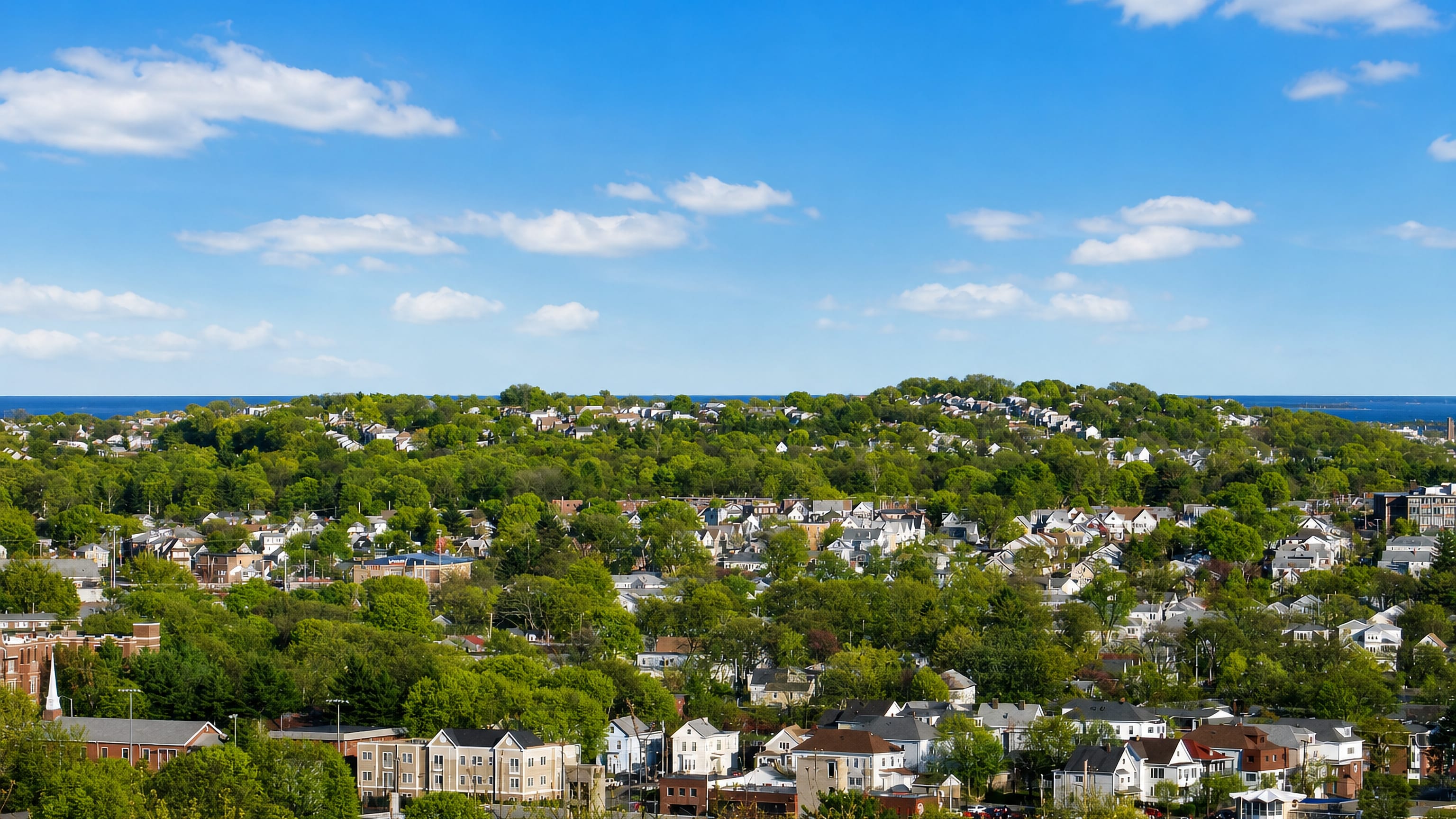 Wooded hillside of clapboard houses in Revere, Massachusetts, with the Atlantic Ocean on the horizon.
