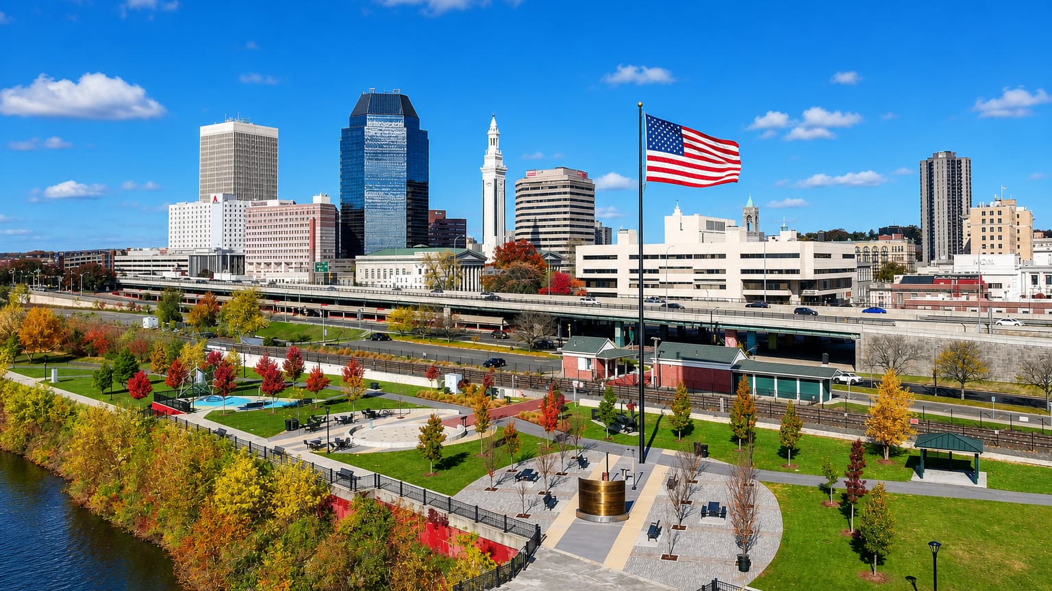 Springfield, Massachusetts, skyline with the Campanile and glass towers seen from a riverfront park flying a US flag.