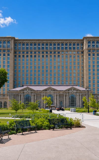 Michigan Central Station towering over a landscaped park in Corktown, Detroit, under a blue summer sky