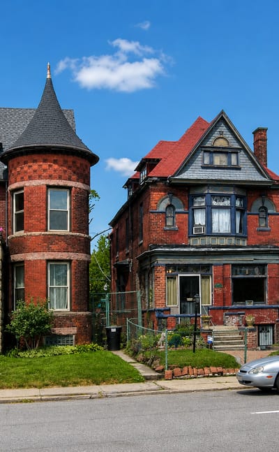 Ornate Victorian brick houses with a turret line a residential street in Detroit's Woodbridge Historic District.