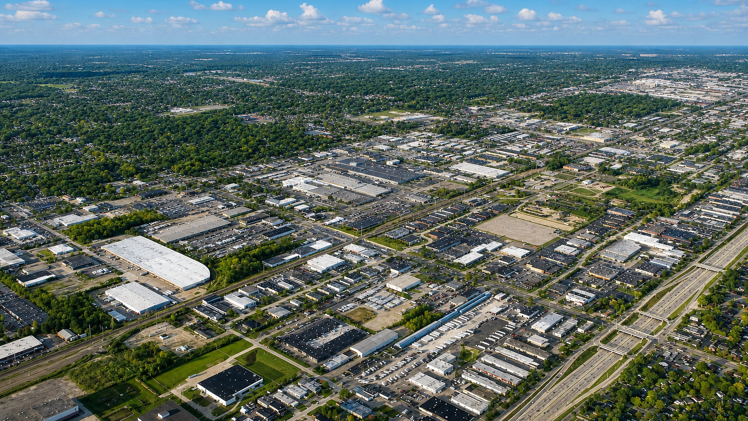 Aerial view of Livonia, Michigan, showing low-rise industrial parks, tree-lined suburbs and a freeway corridor.