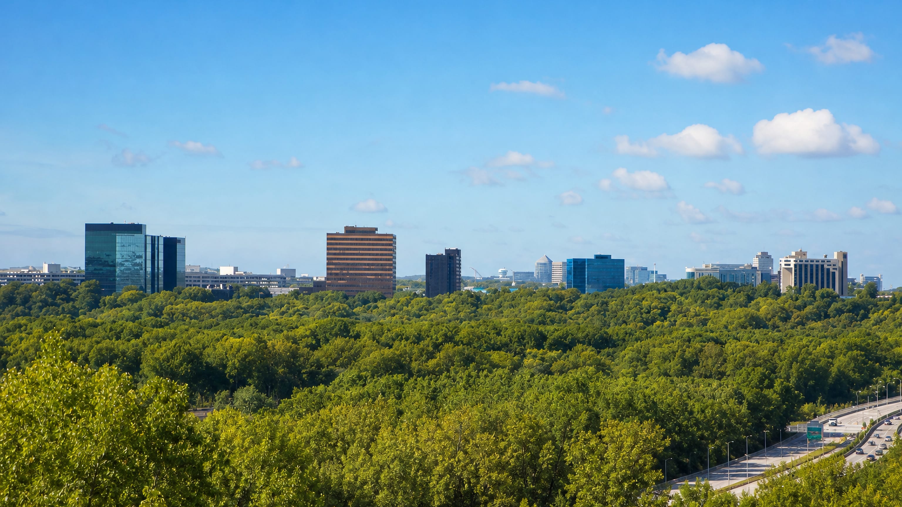 Bloomington, Minnesota, glass and brick office towers rising above a dense tree canopy beside the interstate.