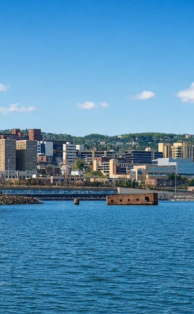 Duluth, Minnesota's hillside downtown rising above Lake Superior, seen past a rocky breakwater.