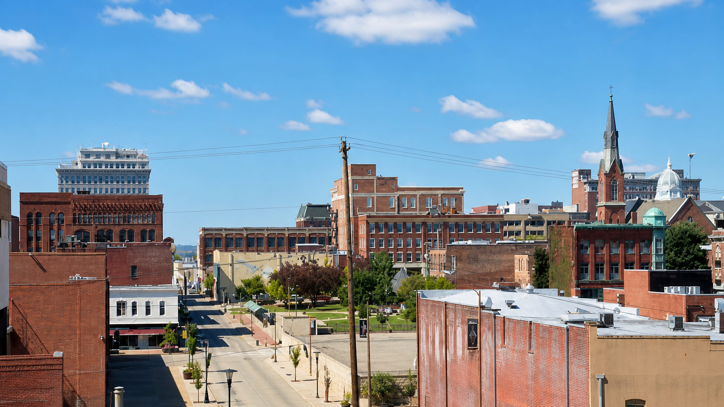 Rooftop view over downtown Saint Joseph, Missouri, with red-brick blocks, a church spire and a domed landmark.