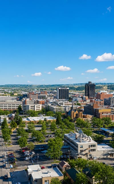 Downtown Billings, Montana with a high-rise tower and the sandstone Rimrocks cliffs beyond a tree-lined boulevard.