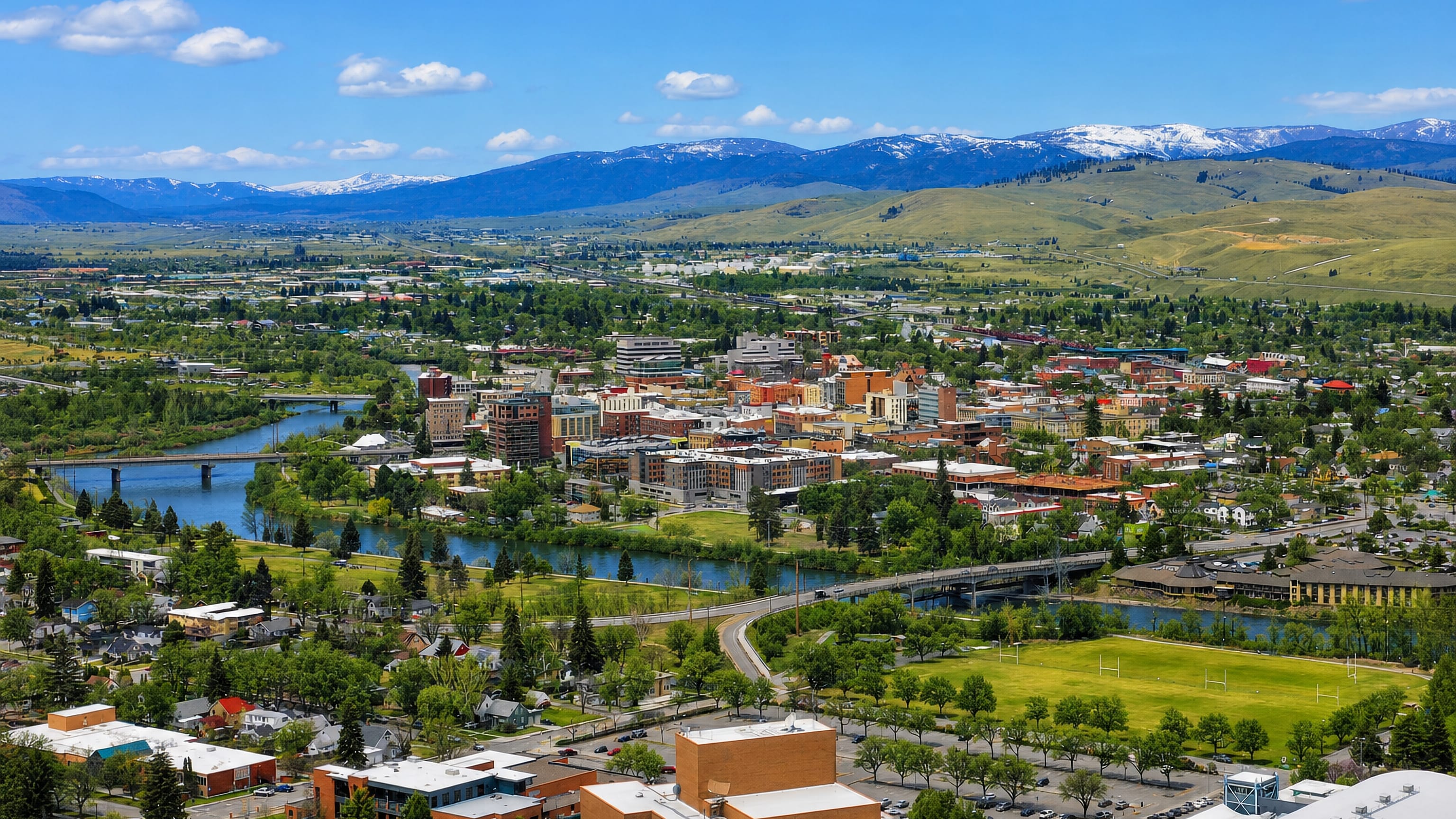 Downtown Missoula, Montana, along the Clark Fork River with snow-capped mountains beyond.