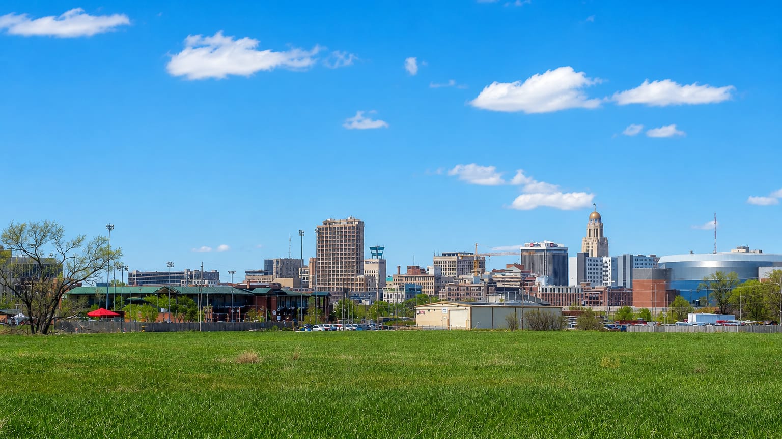 Lincoln, Nebraska skyline across a green field, with the Nebraska State Capitol tower at center.
