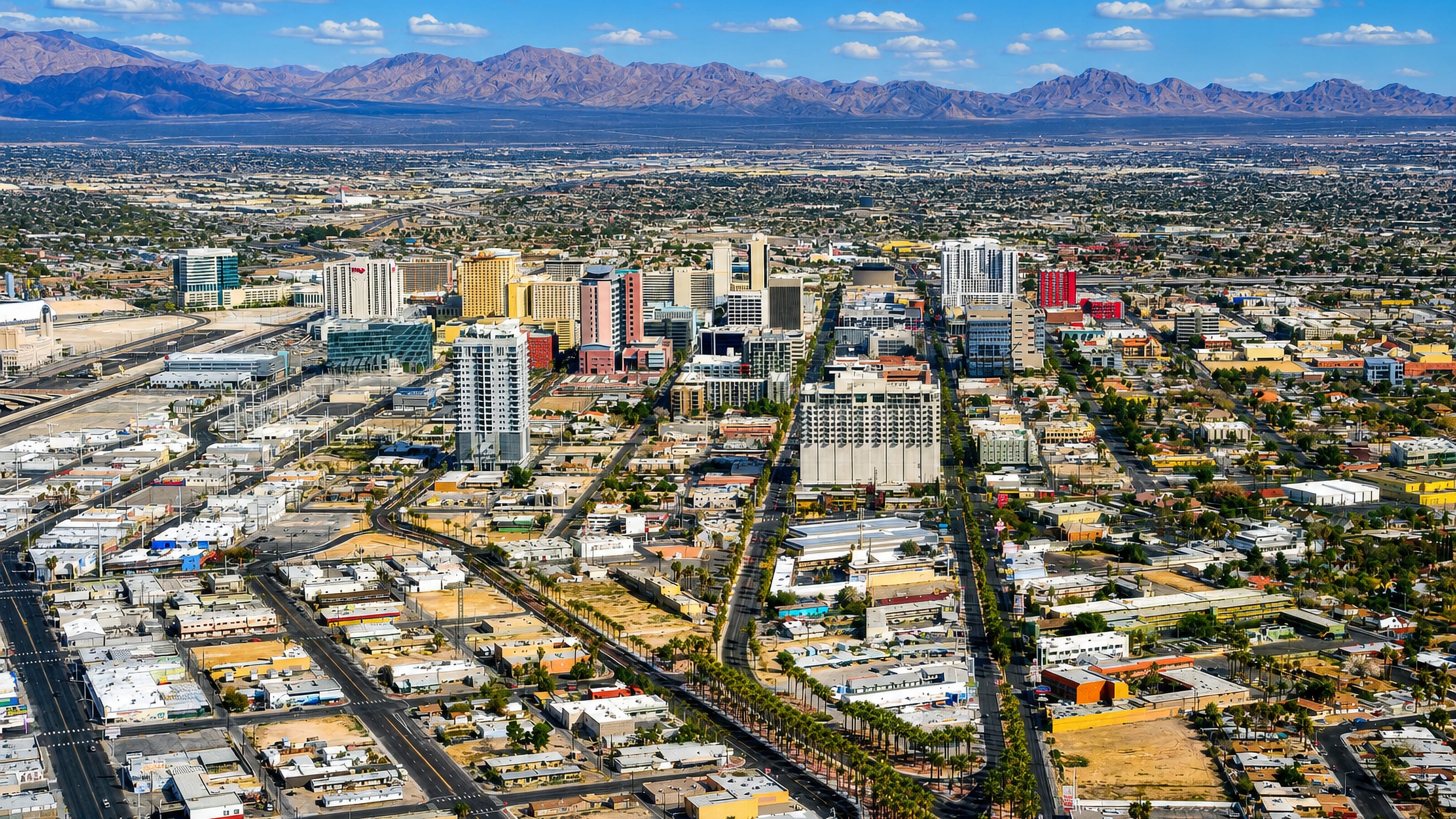 Aerial view of Downtown Las Vegas, with Fremont Street casino towers, palm-lined boulevards and desert mountains.