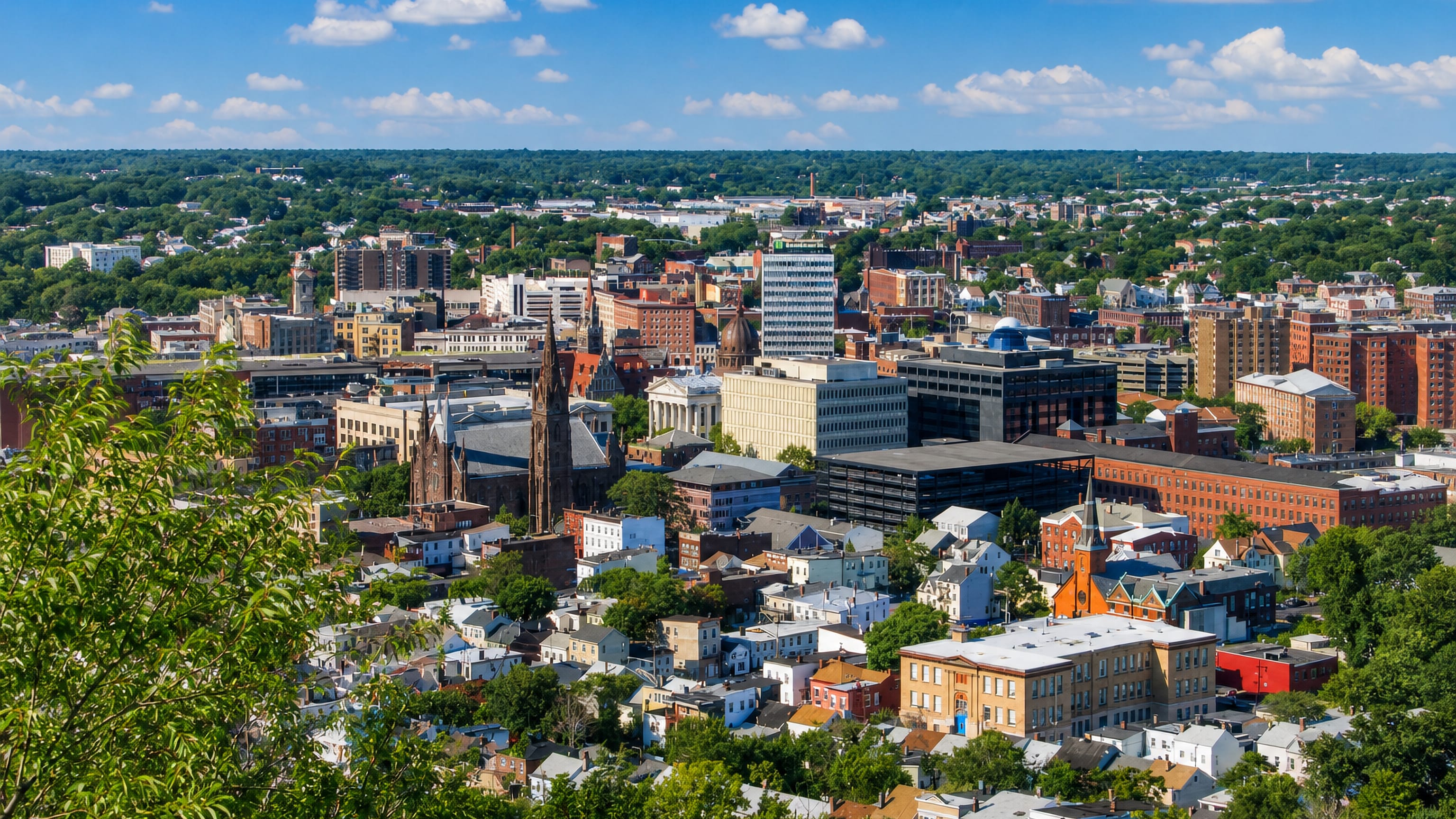 Hillside view over downtown Paterson, New Jersey, with brick mill blocks, a Gothic church spire and a domed courthouse.