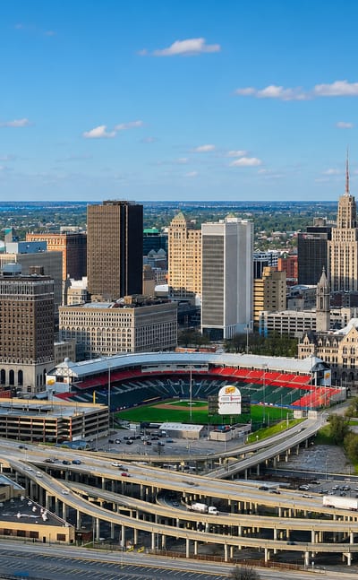 Aerial view of downtown Buffalo, New York, with the M&T Center tower, ballpark and highway interchange under a blue sky.