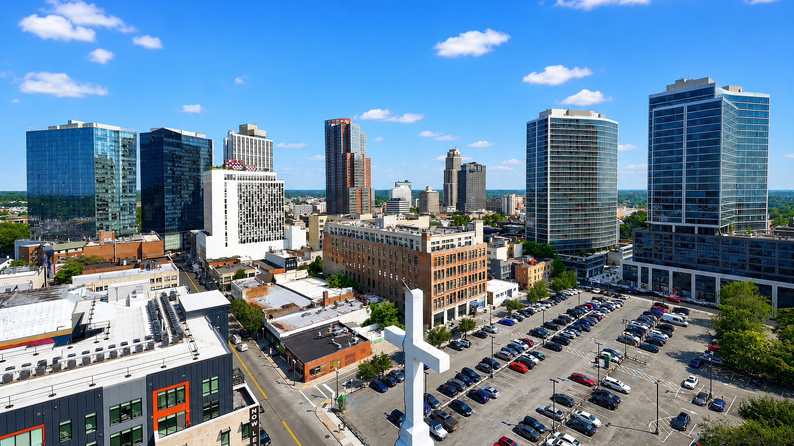 New Rochelle's downtown glass towers and low brick blocks seen from above, with a church cross in the foreground.