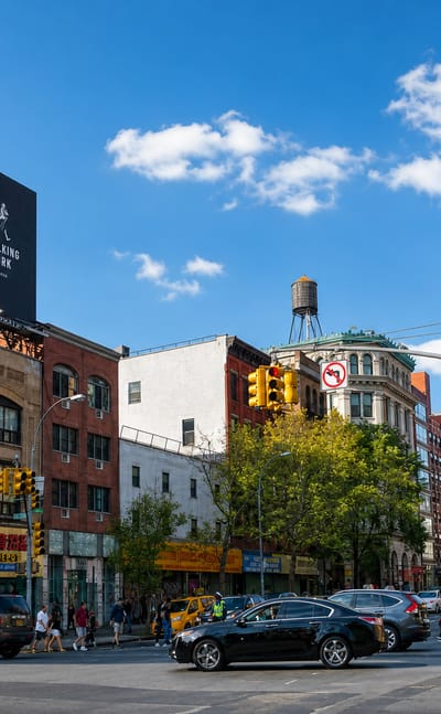 Busy Bowery street corner beside Manhattan's Chinatown with brick buildings, shop signs and a rooftop water tower.