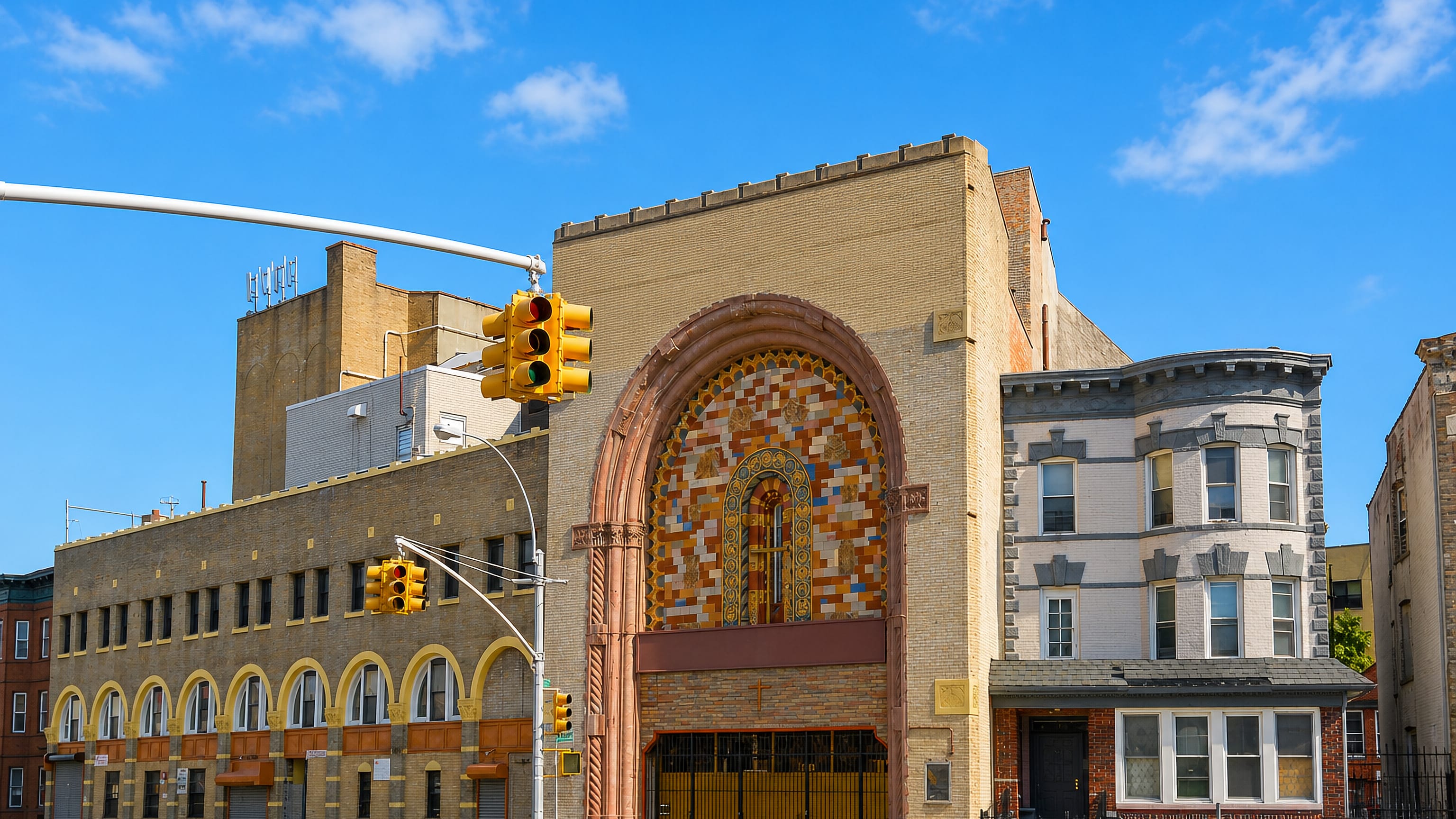 A Brownsville street corner in Brooklyn, with an arched mosaic-fronted brick hall beside older walk-up houses.