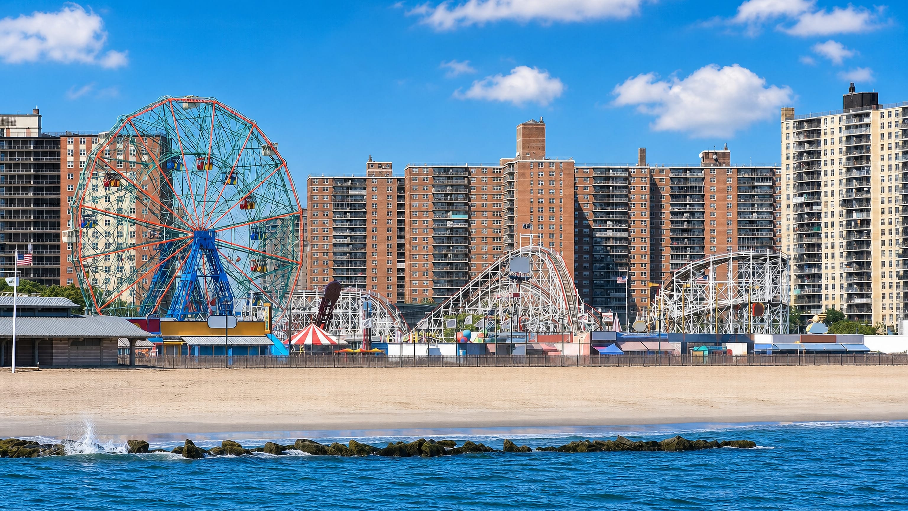Coney Island's Wonder Wheel and Cyclone coaster behind the beach and brick apartment towers in Brooklyn.