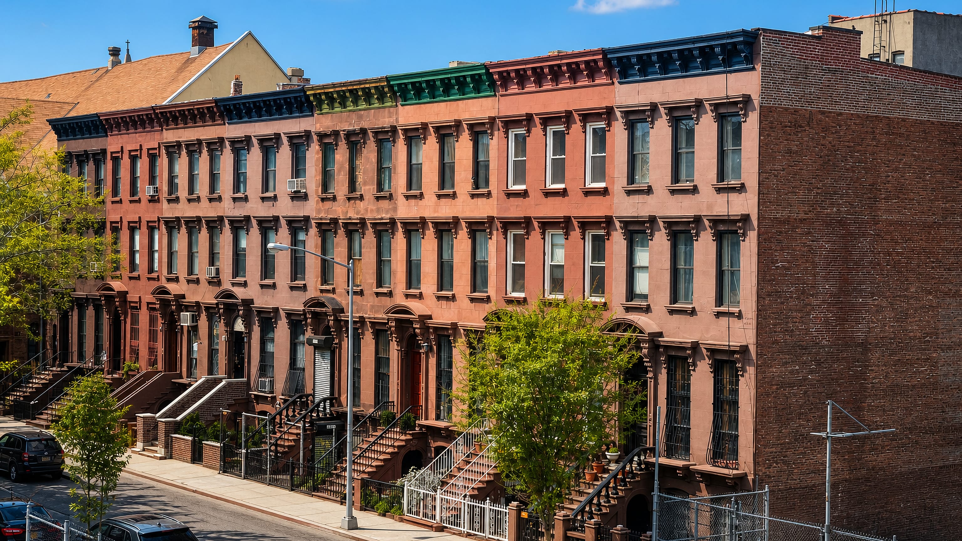 A row of brownstones with colourful cornices and stoops on a sunlit East Harlem street in New York.