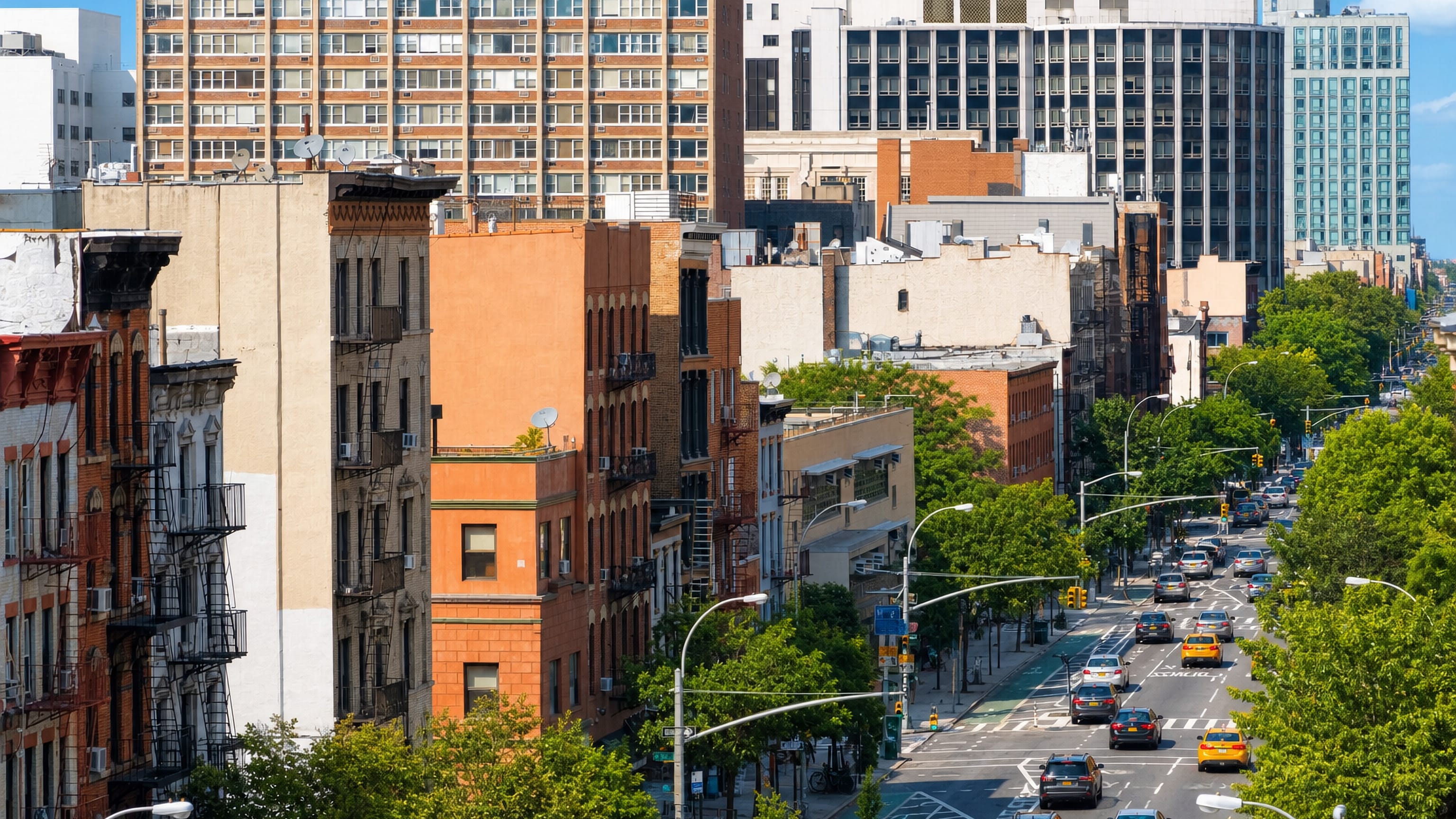 Tenement rooftops and fire escapes above a tree-lined avenue in Manhattan's East Village