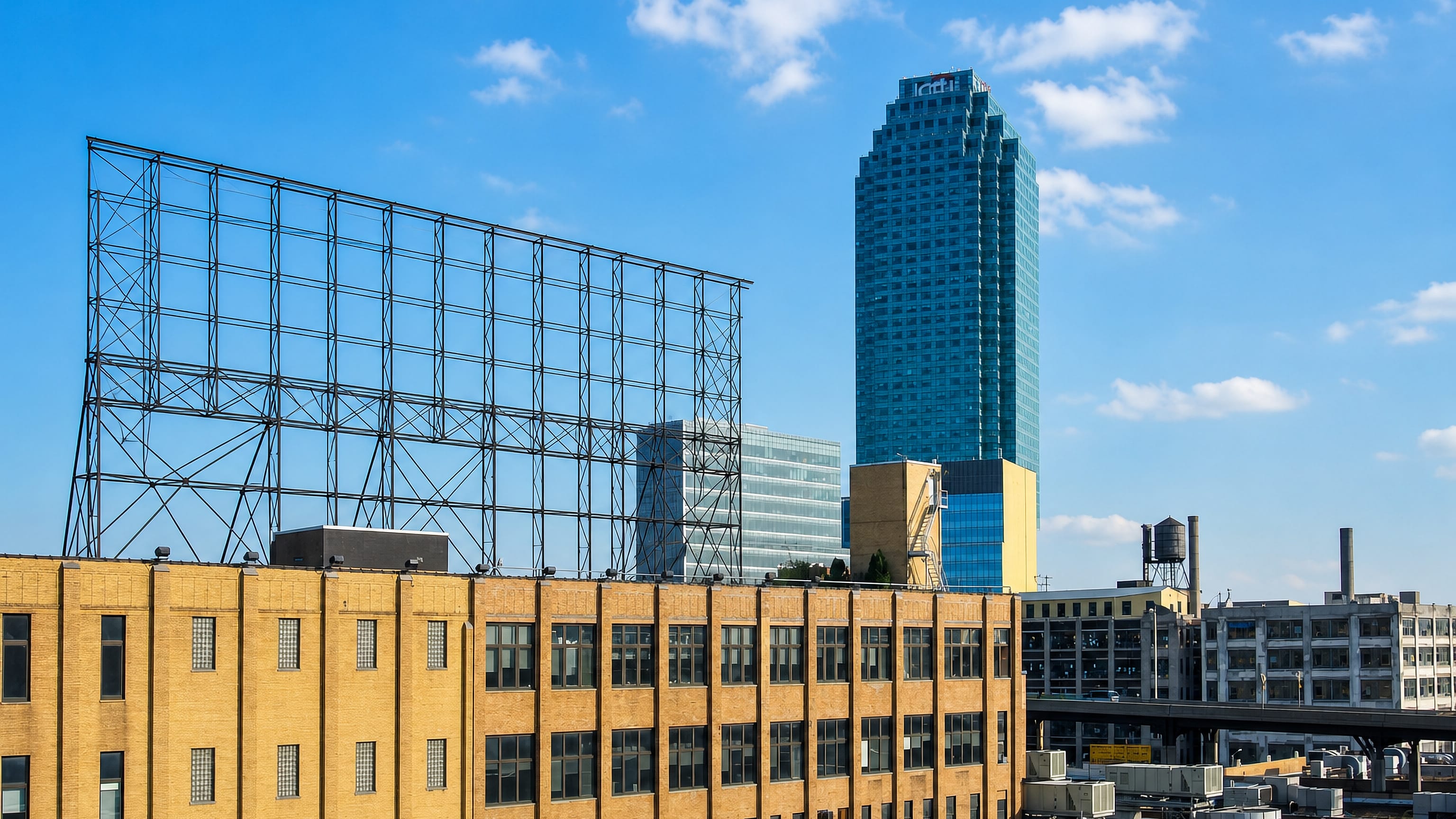 One Court Square's blue glass tower rising above Long Island City warehouses and a bare billboard frame.