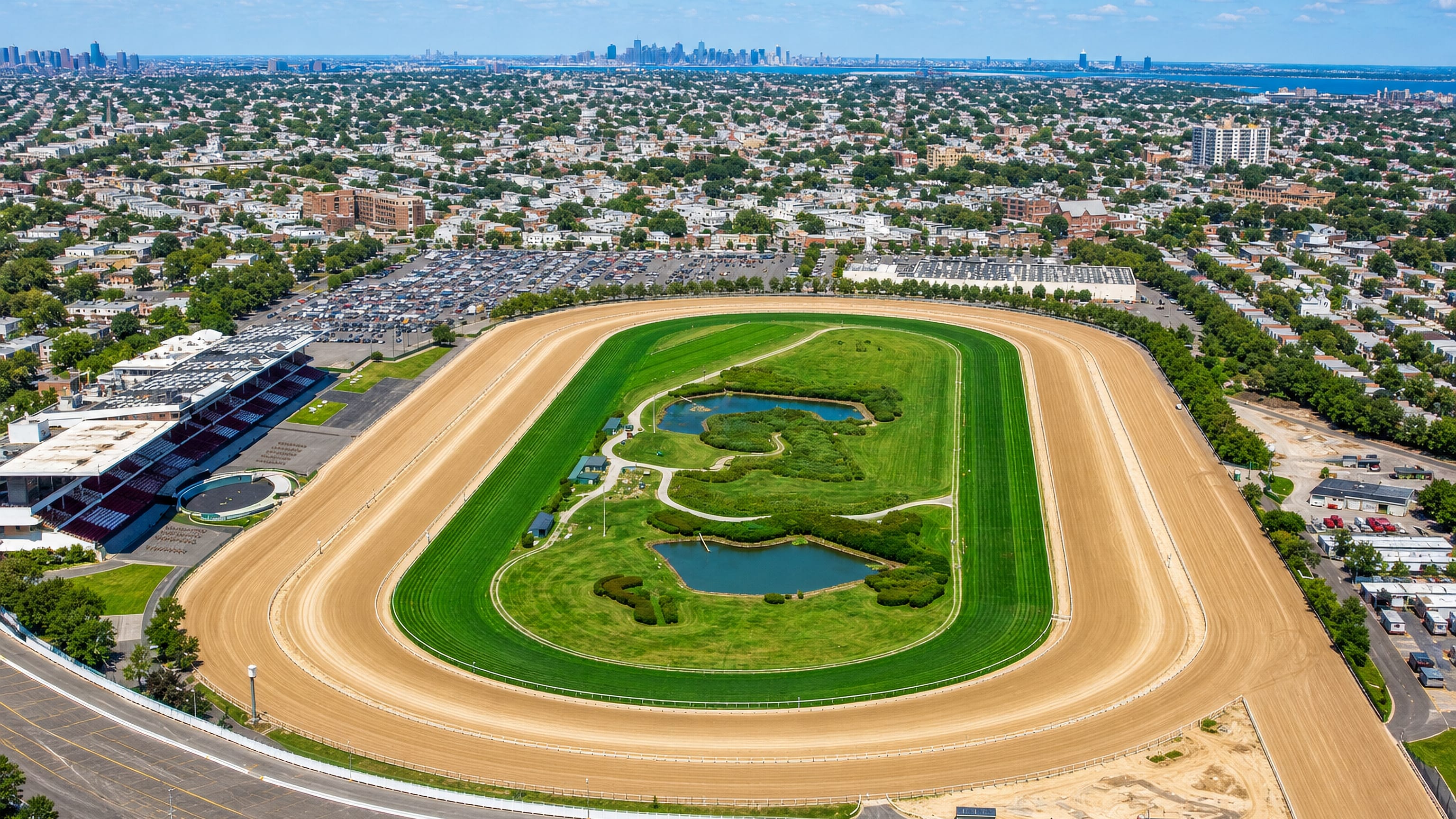 Aerial view over Aqueduct Racetrack and the rowhouse streets of Ozone Park, Queens, with the Manhattan skyline beyond.