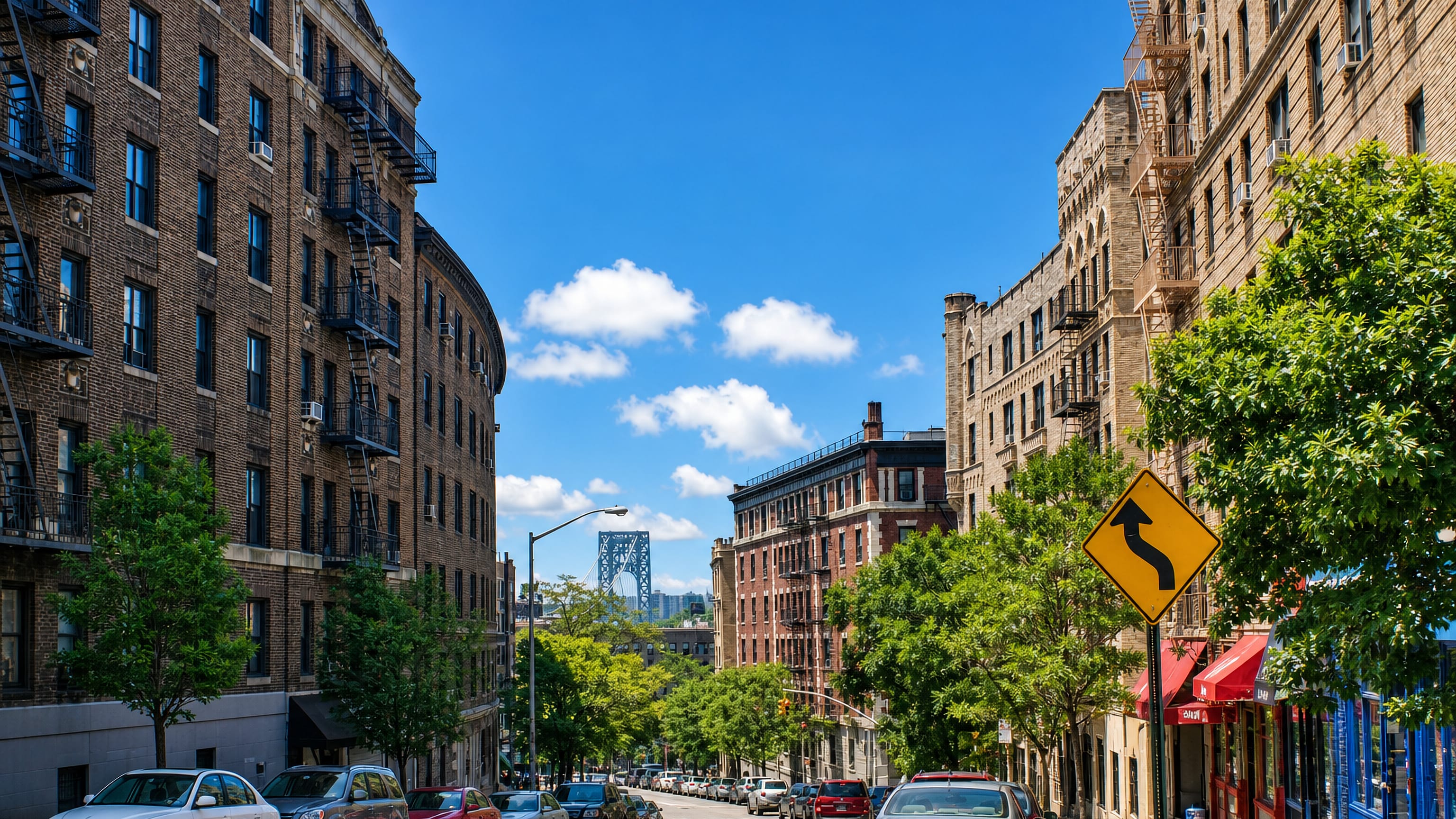 Prewar apartment blocks line a Washington Heights street in Manhattan, with the George Washington Bridge at its end.