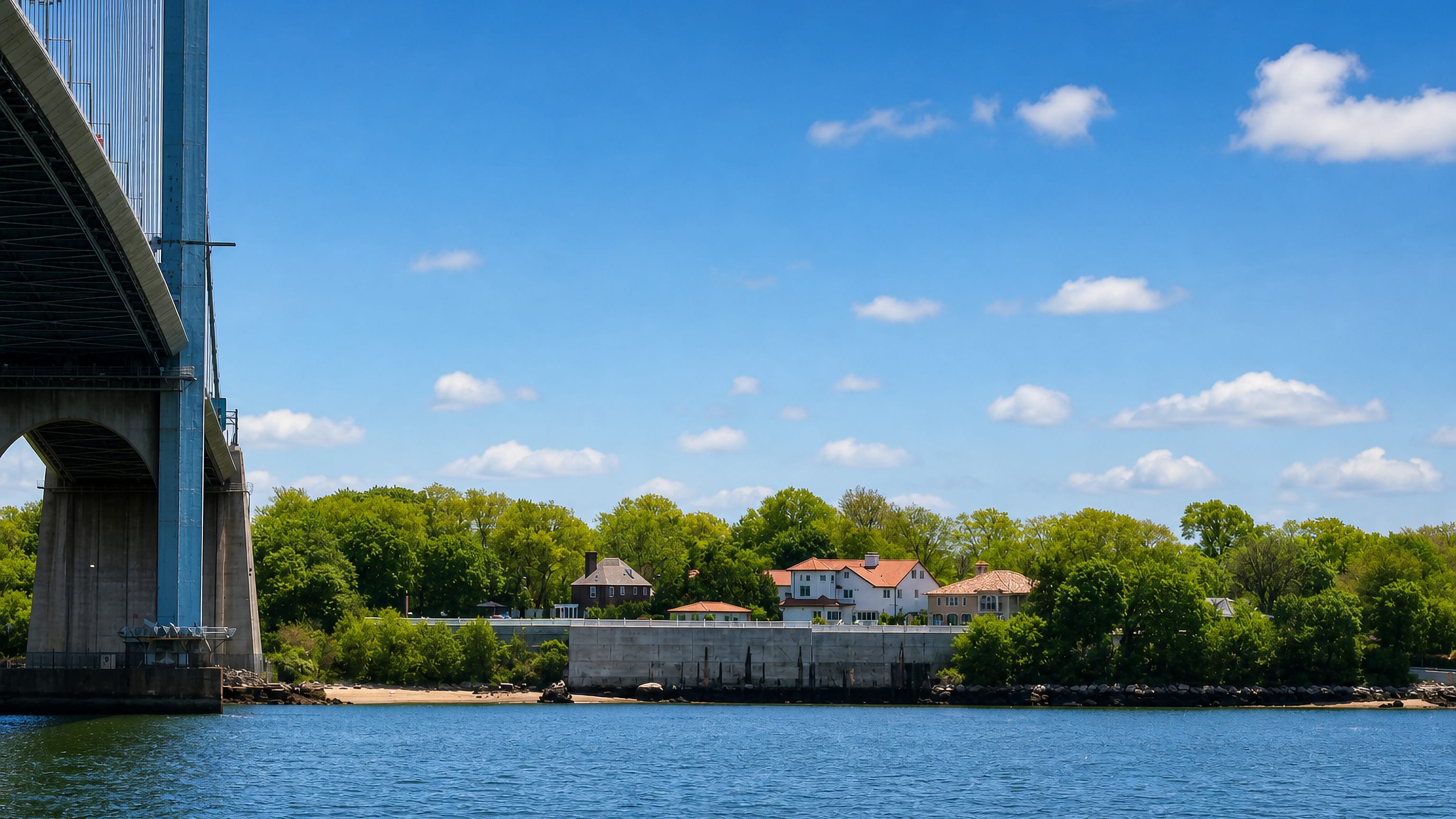 The Bronx-Whitestone Bridge rises over the water beside Whitestone's wooded shoreline in Queens, New York.