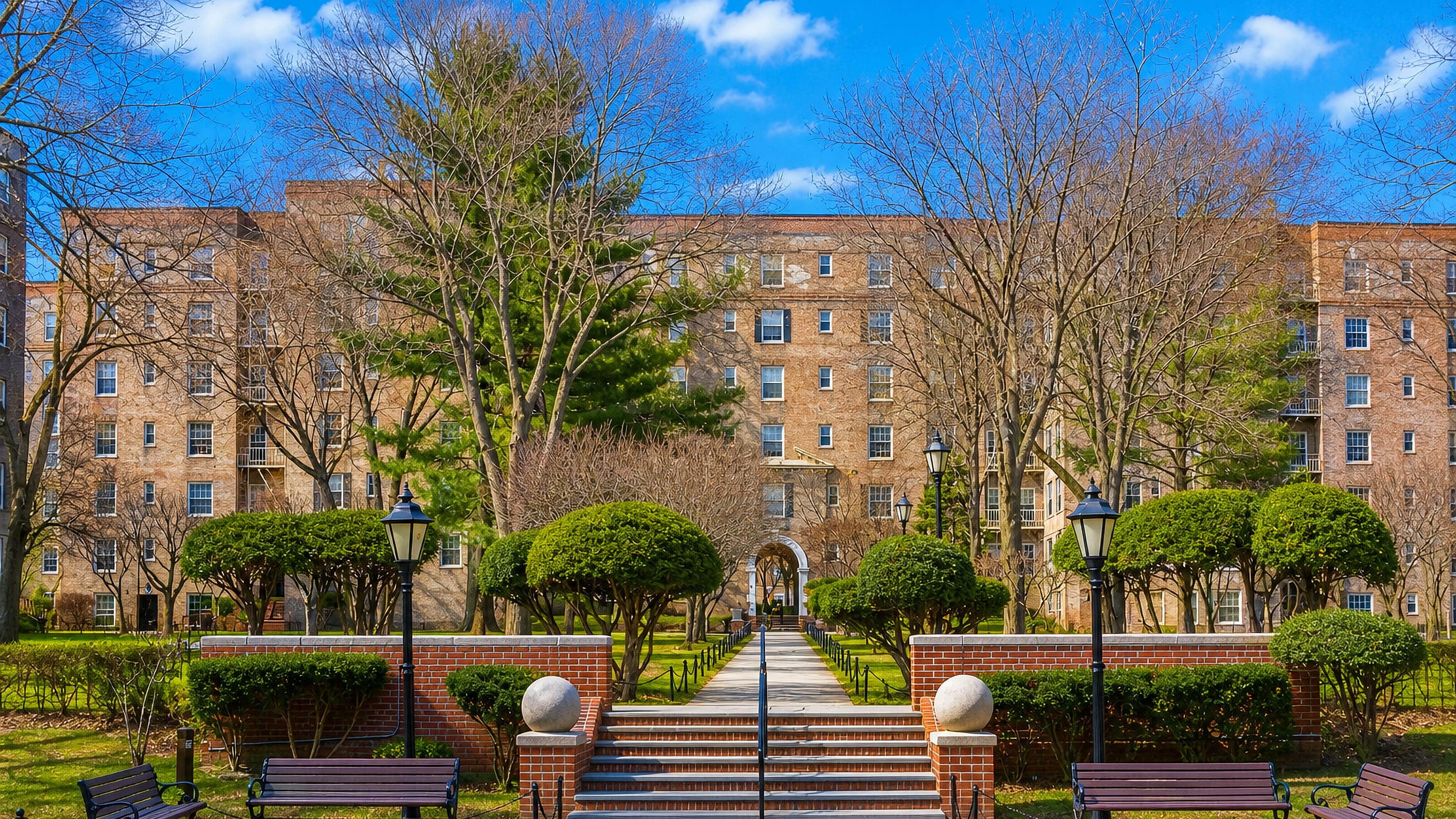 Brick garden-apartment blocks around a landscaped courtyard with benches and clipped hedges in Woodside, Queens.