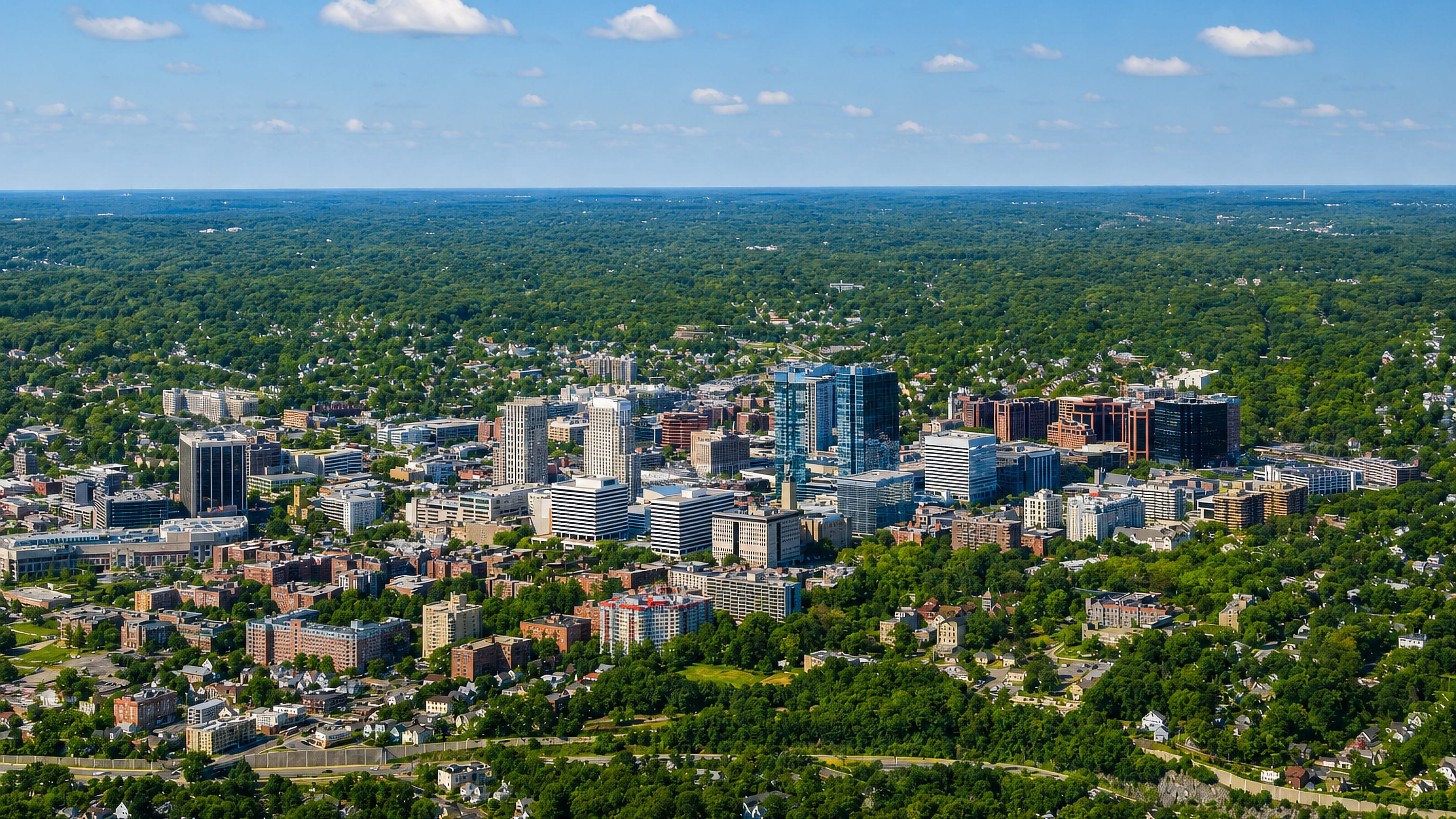 Aerial view of downtown White Plains, New York, its office towers rising from Westchester's wooded suburbs.