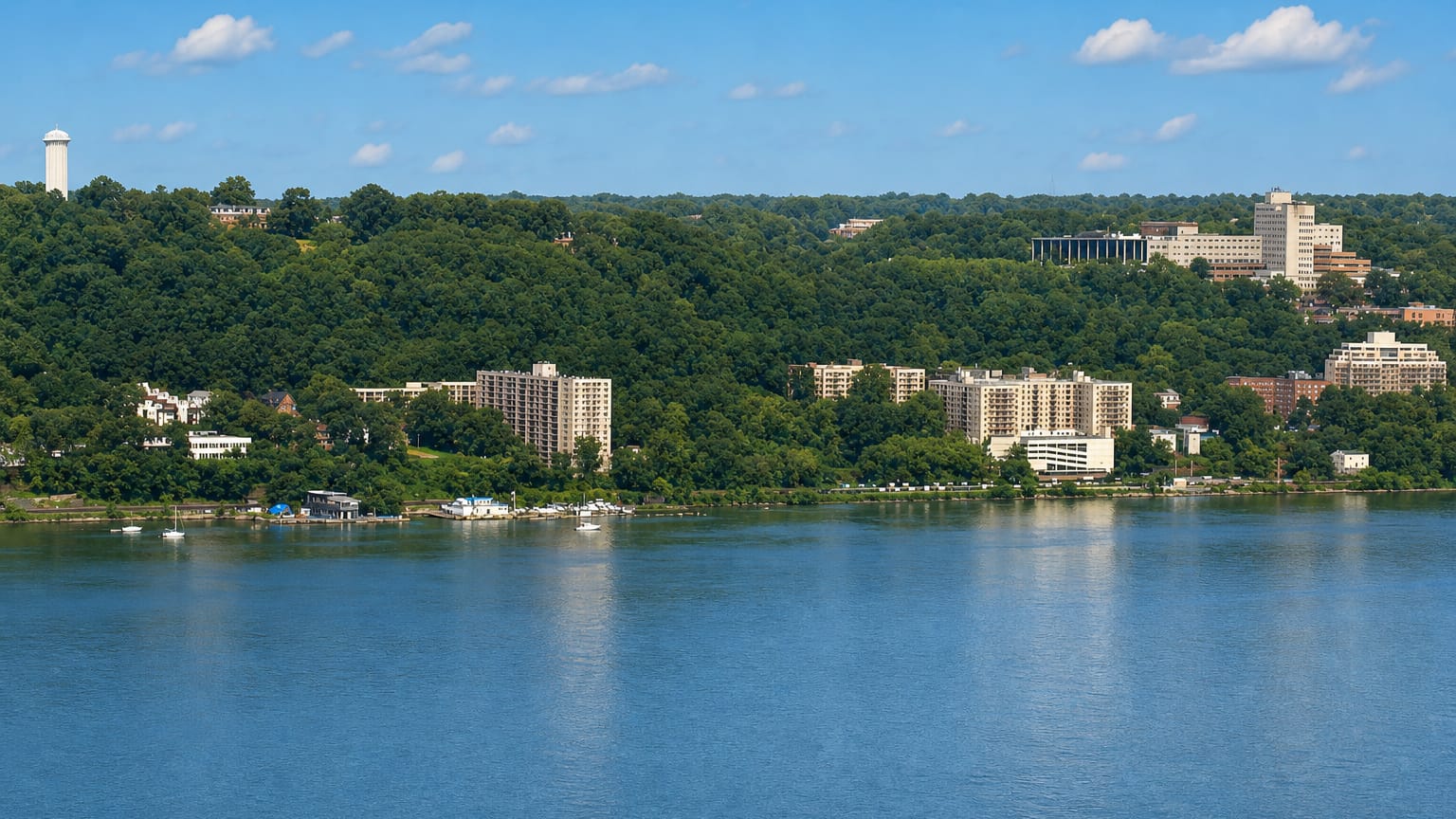 Wooded Hudson River bank with apartment towers and a hilltop water tower at Yonkers, New York.