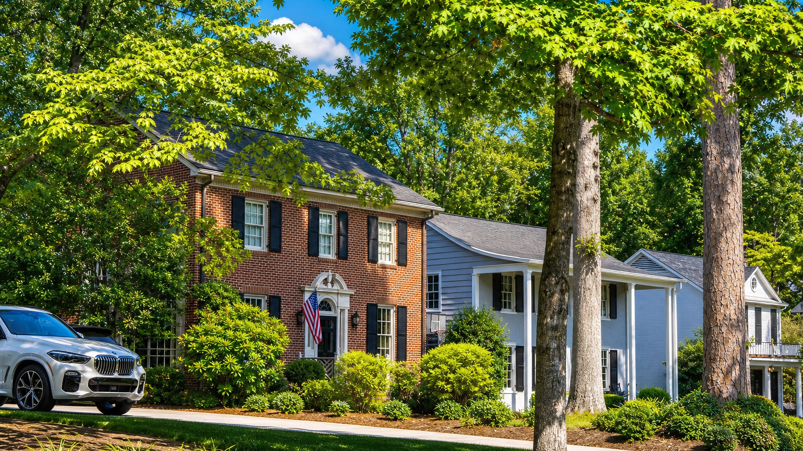 Brick colonial house and white-columned home under a mature oak canopy on a Myers Park street, Charlotte.