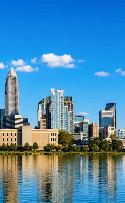 Uptown Charlotte skyline led by the Bank of America crown reflected in still water.