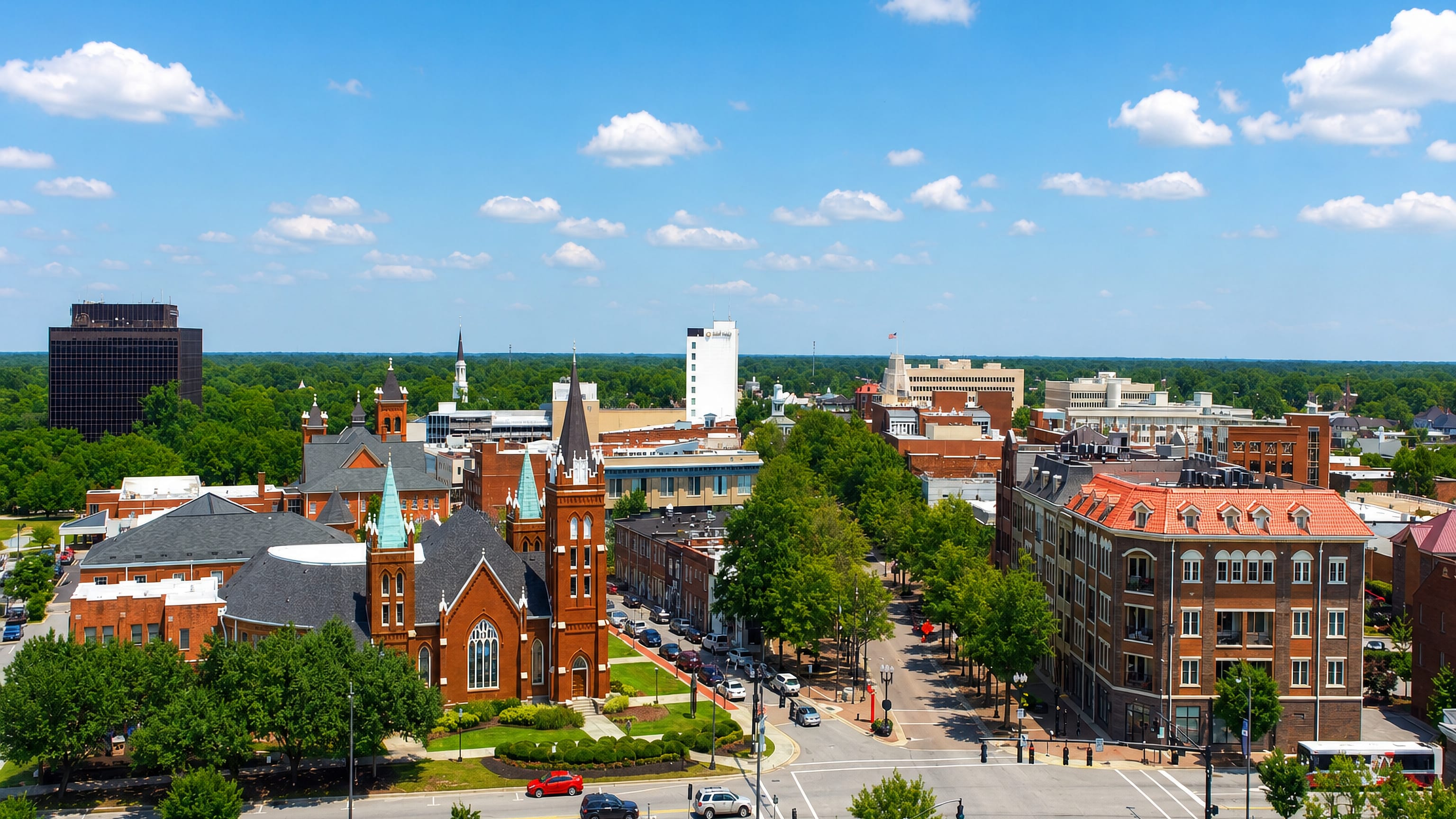 Downtown Fayetteville, North Carolina, with a Gothic brick church, tree-lined main street and a dark glass tower.