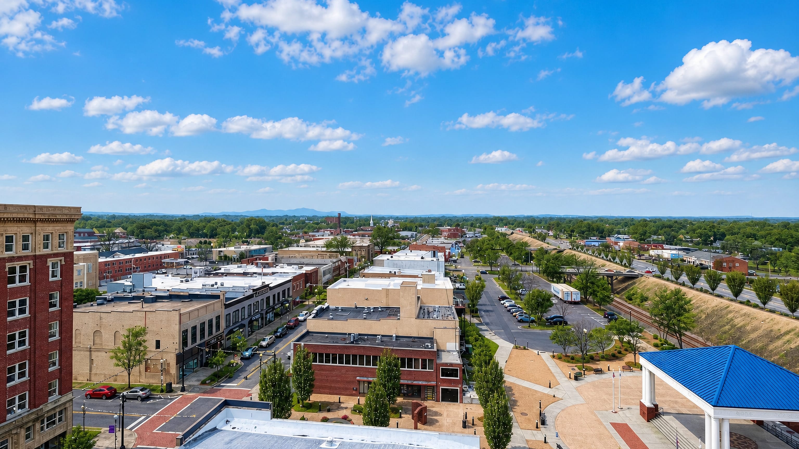 Aerial view of downtown Gastonia, North Carolina, with brick storefronts, a blue-roofed pavilion and distant hills.