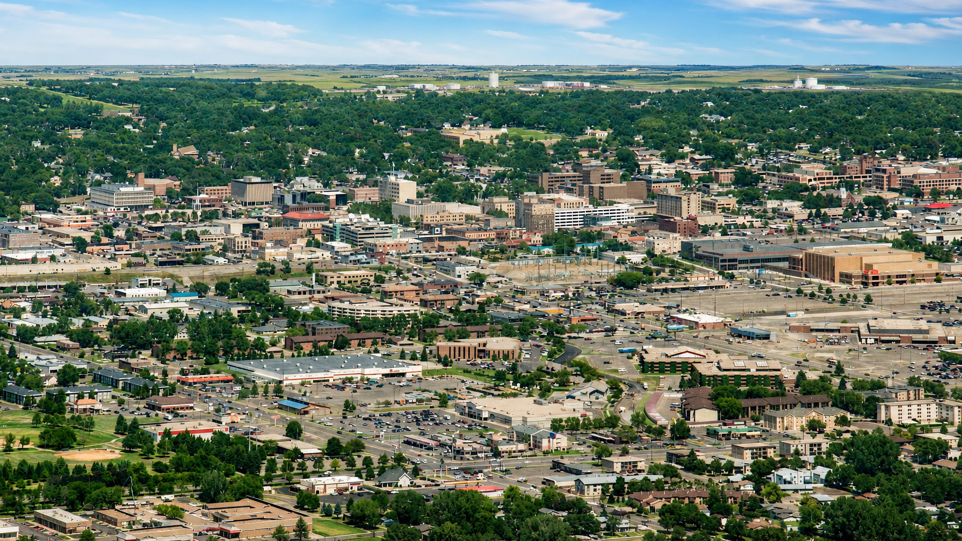 Aerial view over downtown Bismarck, North Dakota, its low-rise blocks and leafy streets meeting open prairie.