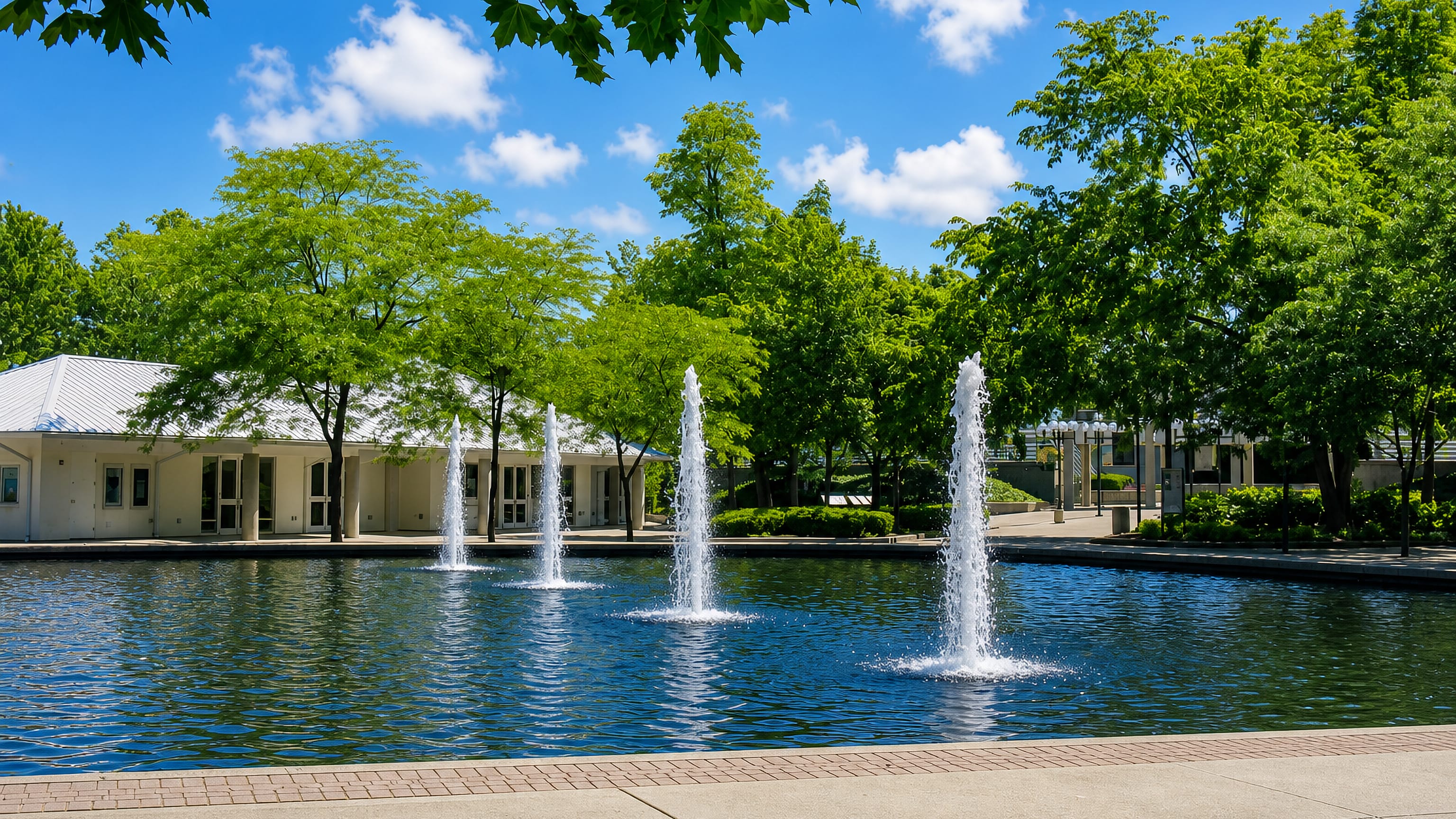 Fountain jets in a park reflecting pool beside a white pavilion in Kettering, Ohio.