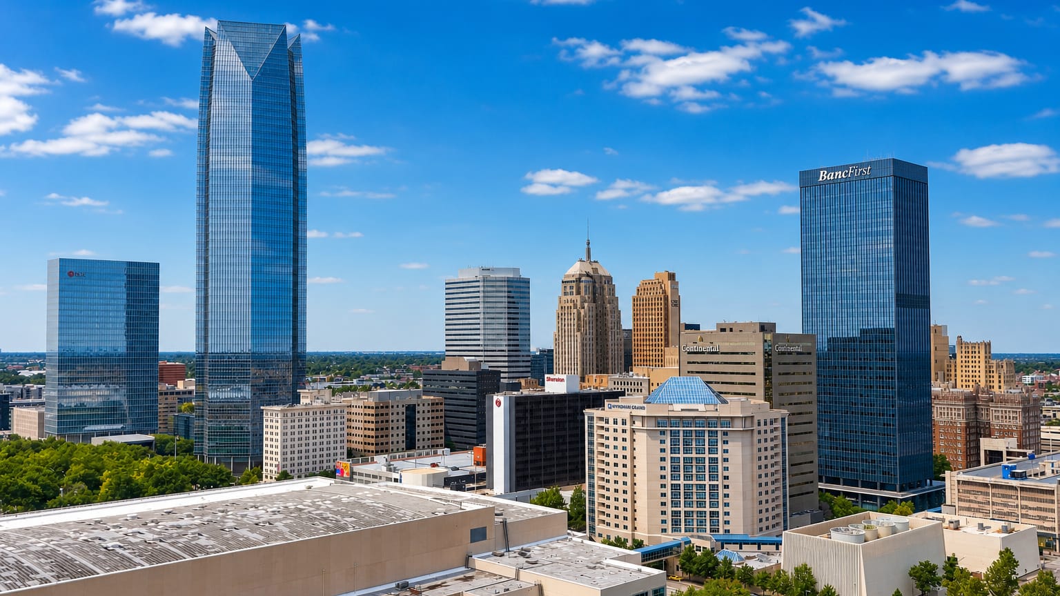Oklahoma City skyline led by the pointed Devon Tower and glass high-rises under a bright blue sky.