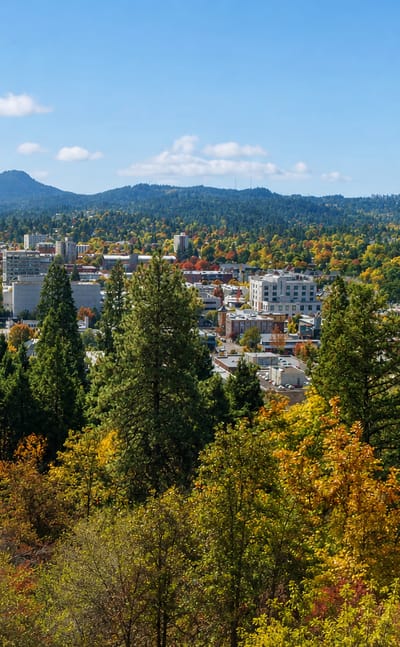 Downtown Eugene, Oregon framed by evergreen forest and autumn foliage with wooded hills behind.