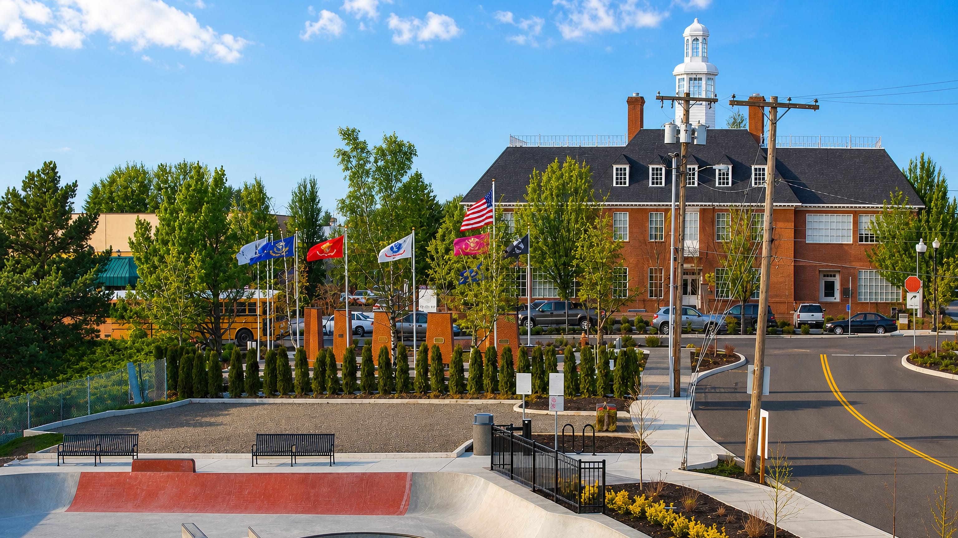 Brick civic building with a white cupola and a row of flags beside a concrete skatepark in Gresham, Oregon