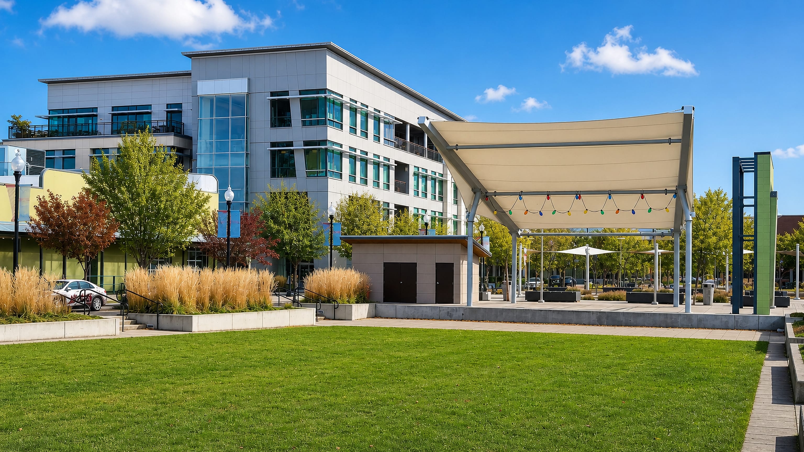 Modern civic building and canopied stage beside a wide lawn in downtown Medford, Oregon.