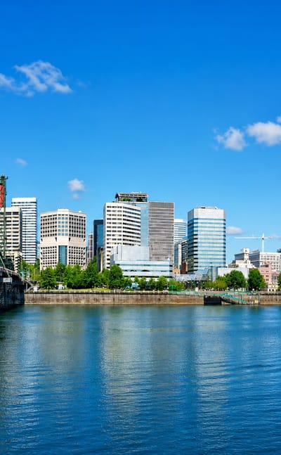 Portland skyline across the Willamette River with the green Hawthorne Bridge and downtown towers under blue sky