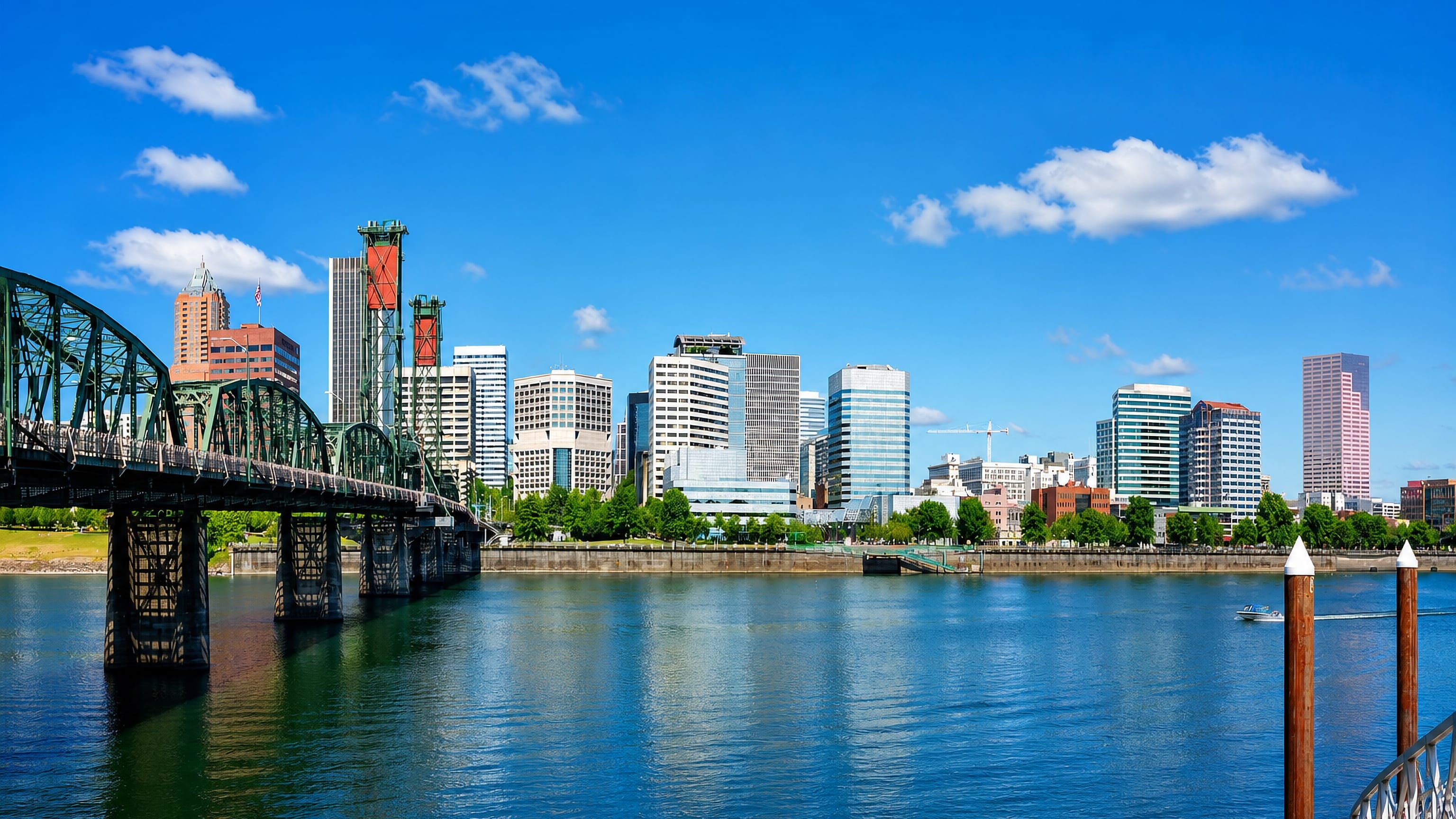 Portland skyline across the Willamette River with the green Hawthorne Bridge and downtown towers under blue sky