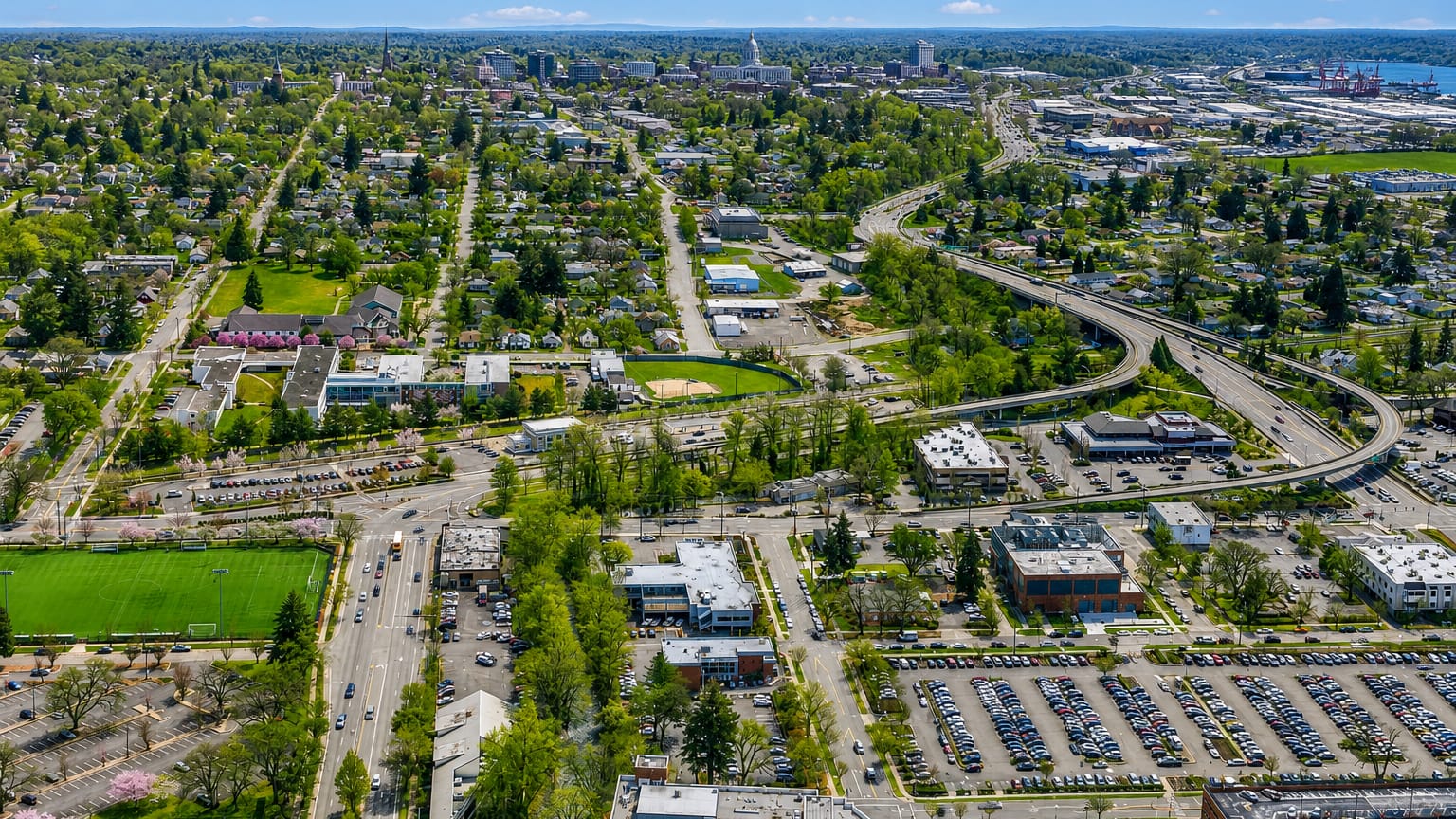 Aerial view of Salem, Oregon with leafy neighborhoods, a curving freeway and the State Capitol in the distance.