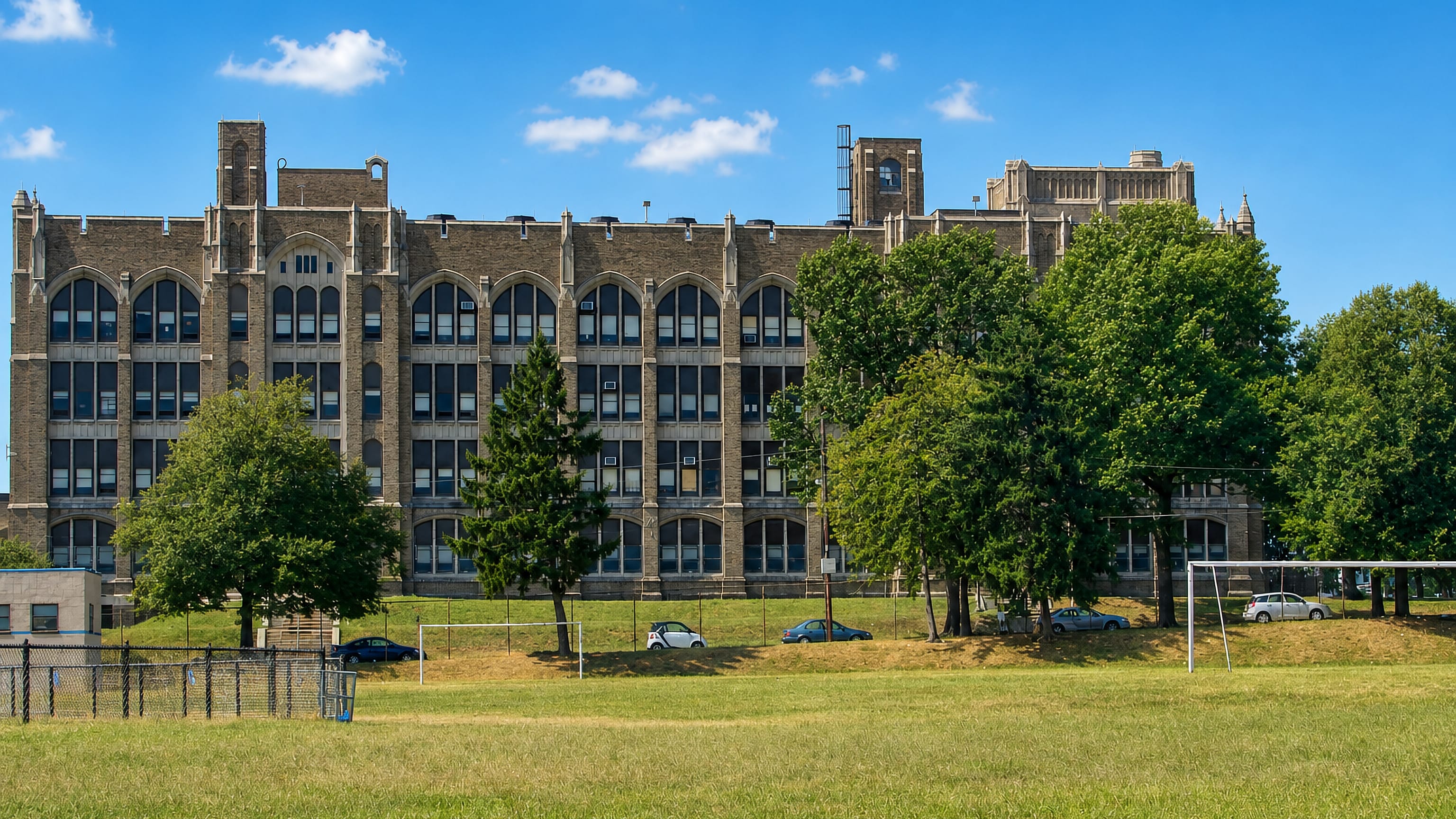 Gothic-revival school building and open playing field under blue sky in the Olney neighbourhood of Philadelphia.